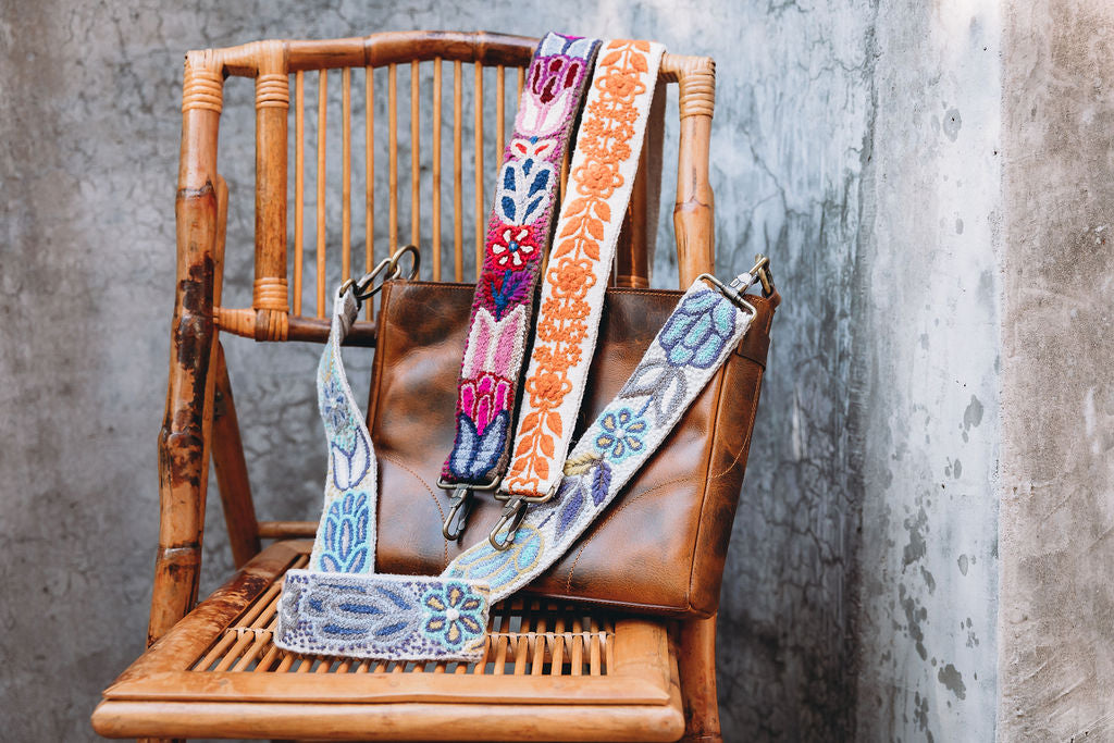 A collection of large hand embroidered colorful purse straps on a chair from Madeline Parks Designs.