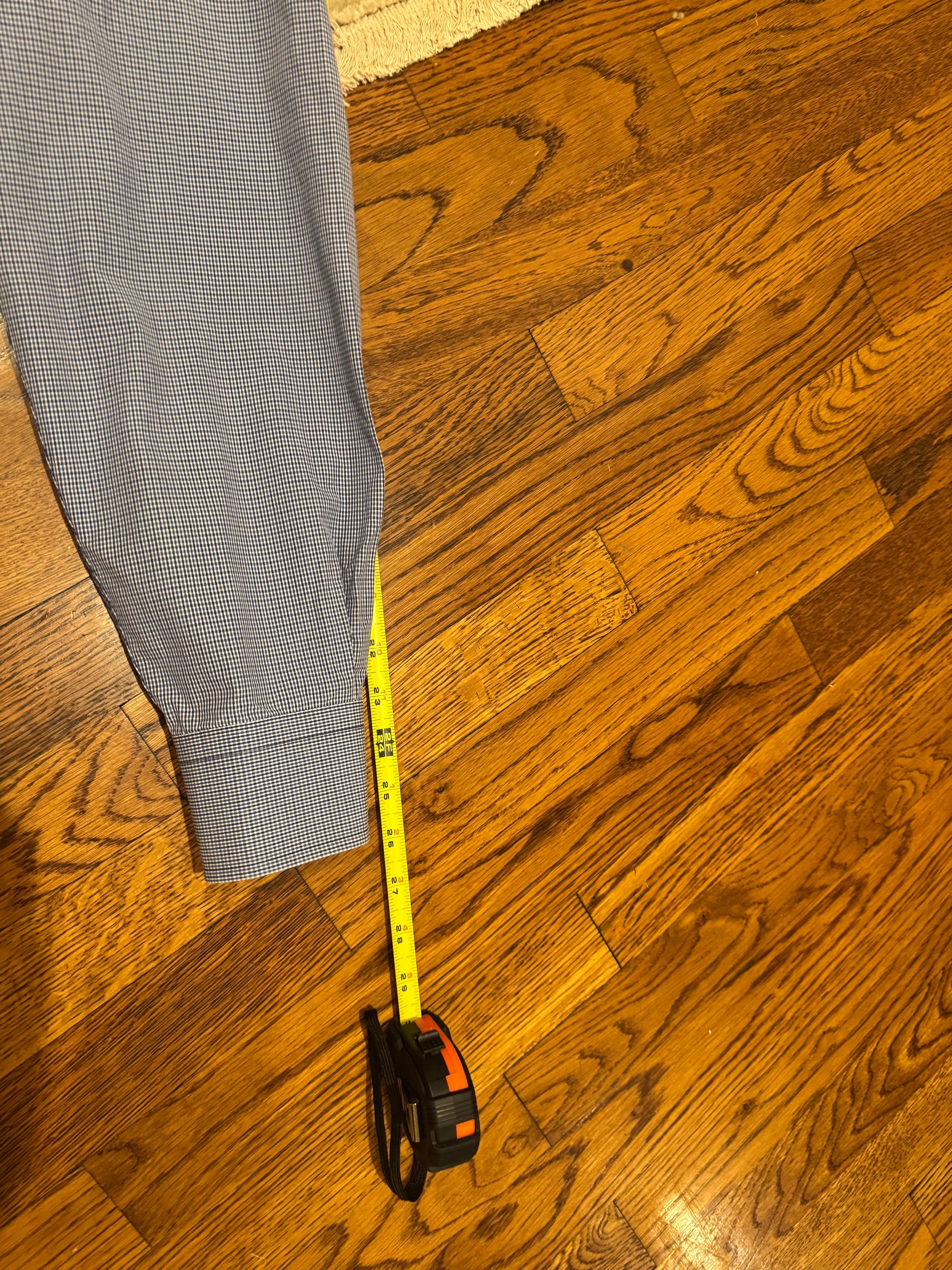Gray patterned trousers laid out on a hardwood floor next to a yellow tape measure.