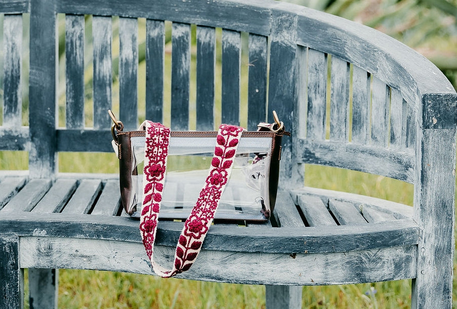 Clear purse with strap shown on a bench.