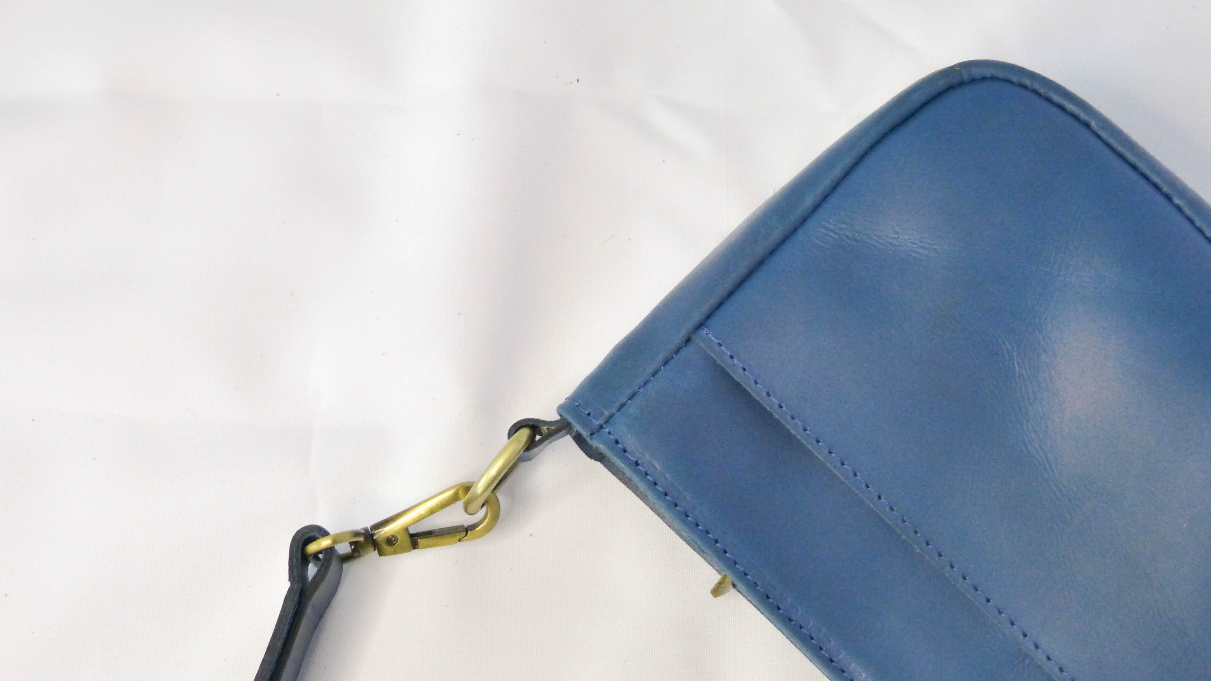 A blue leather purse with a gold chain, the Jessica Leather Purse in Cornflower Blue by Madeline Parks Designs. Features a zippered top, inside zipper pocket, and removable shoulder strap. Handmade by Ethiopian artisans.