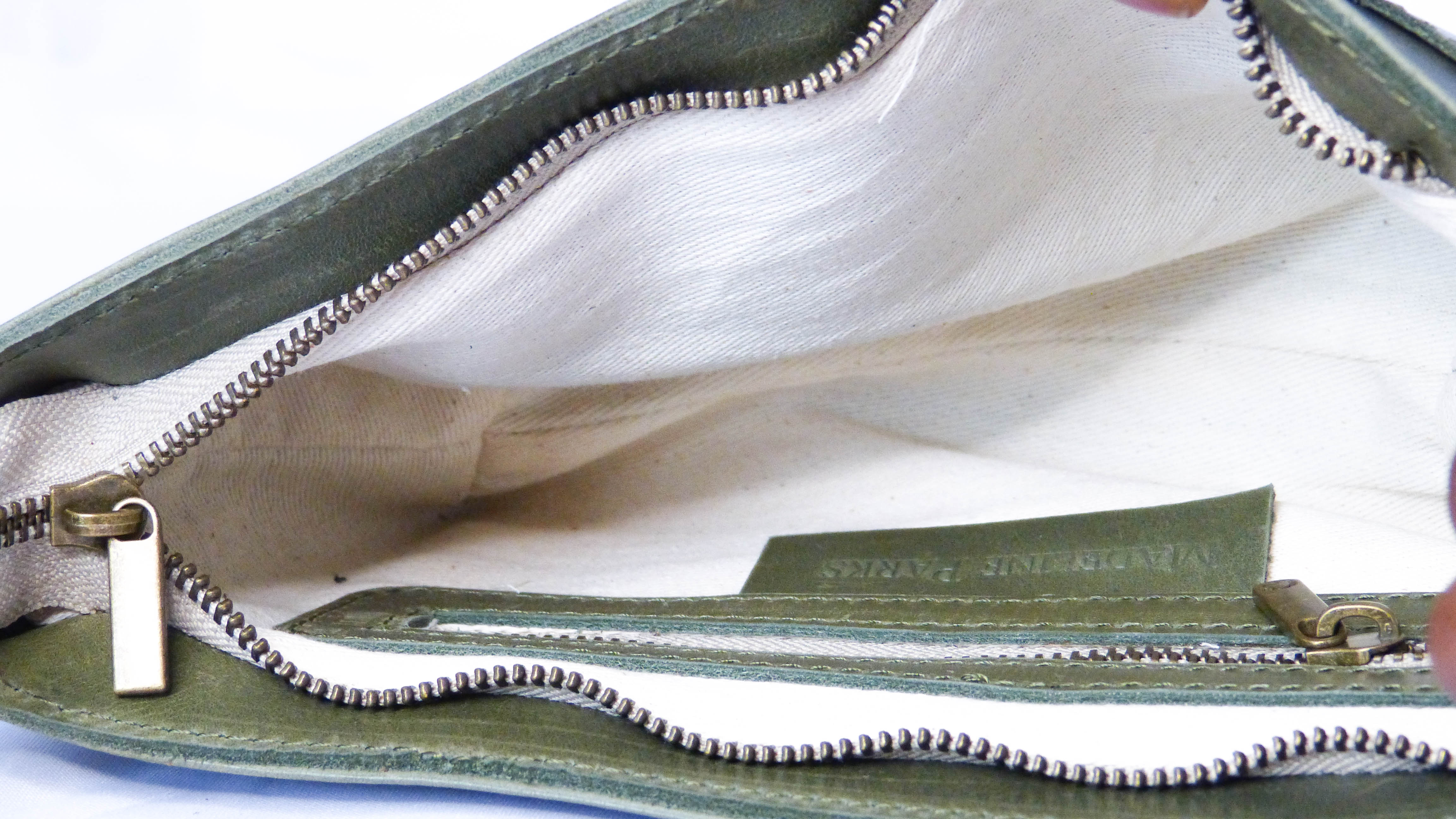 Close-up of the Jessica Leather Purse in Olive, showcasing a zipper on soft leather, a removable shoulder strap, inside zipper pocket, and phone pocket. Handmade by Ethiopian artisans.