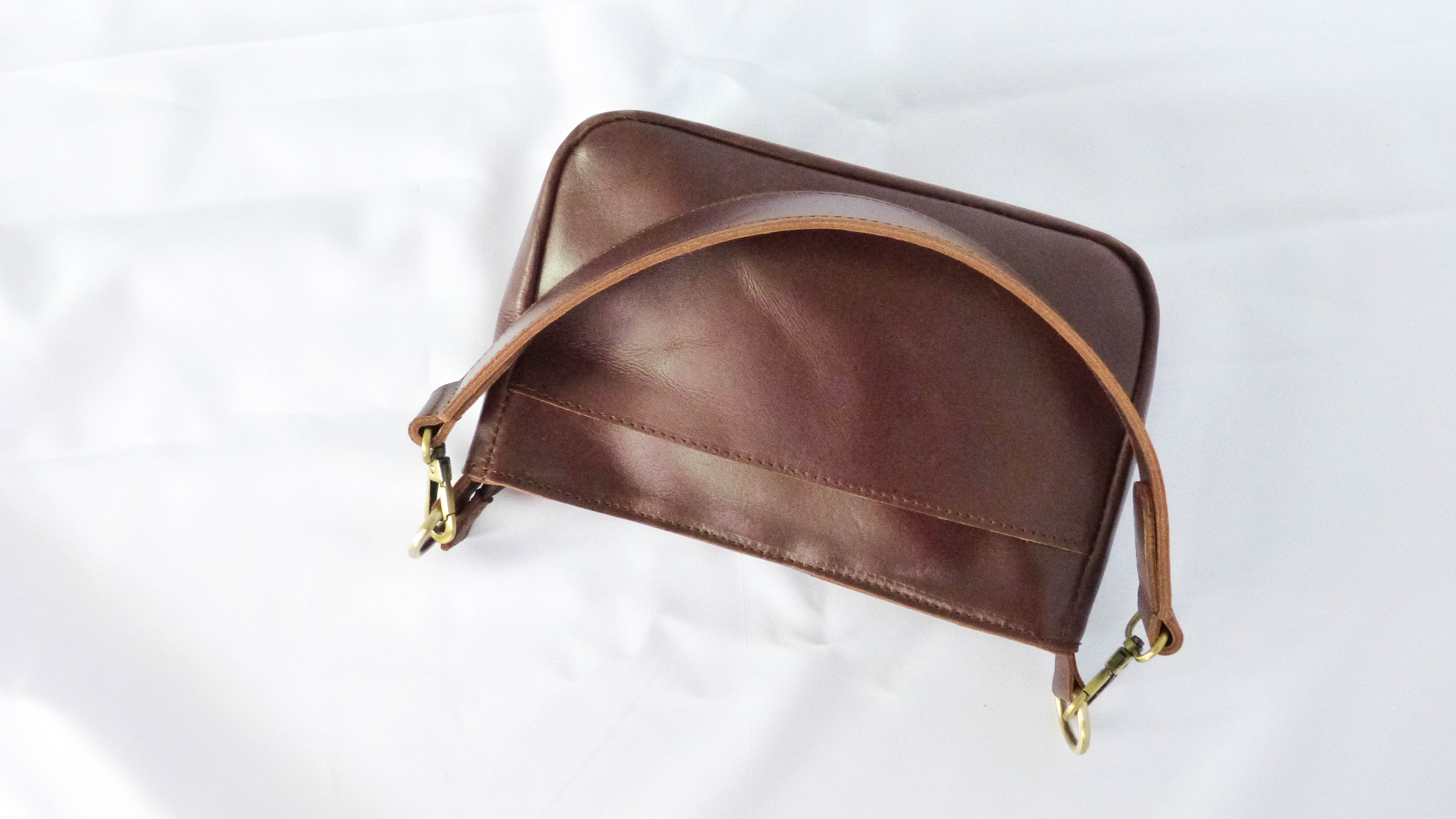 A brown leather Jessica purse with a handle, zippered top, inside zipper pocket, and outside phone pocket. Handmade by Ethiopian artisans, featuring removable shoulder strap for versatile styling.