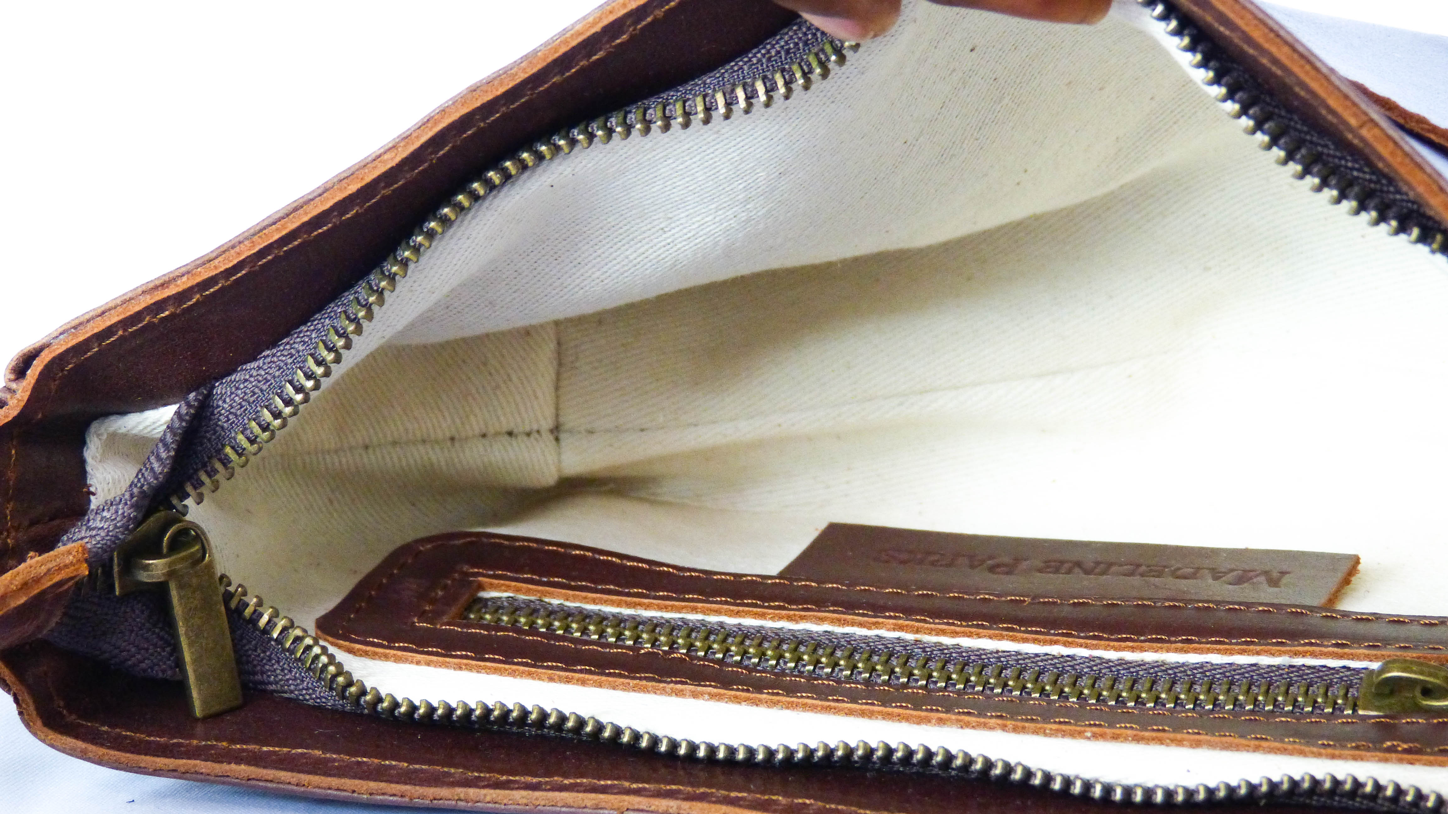 A hand holding a zipper on the Jessica Leather Purse in Whiskey, showcasing artisanal craftsmanship. Features a zippered top, inside pocket, and removable shoulder strap for versatile styling. Handmade by Ethiopian artisans.