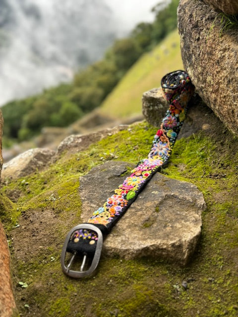 Black Floral Hand Embroidered Belt displayed on a rock, showcasing intricate, hand-loomed wool with vibrant floral embroidery by Andean artisans.