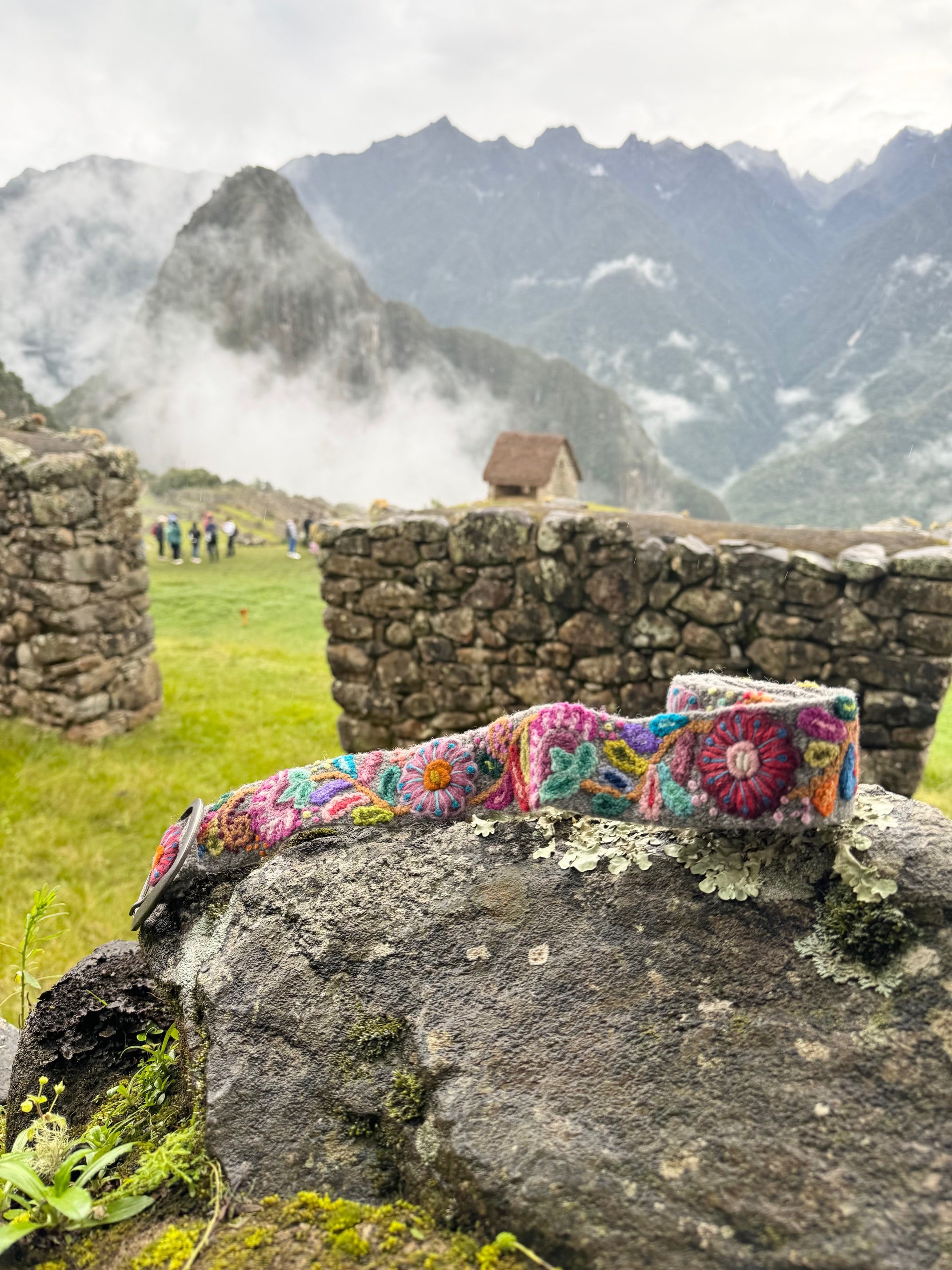 Bright Hand Embroidered Belt on a rock, featuring colorful floral patterns, crafted by Fair Trade artisans in the Andes Mountains of Peru.