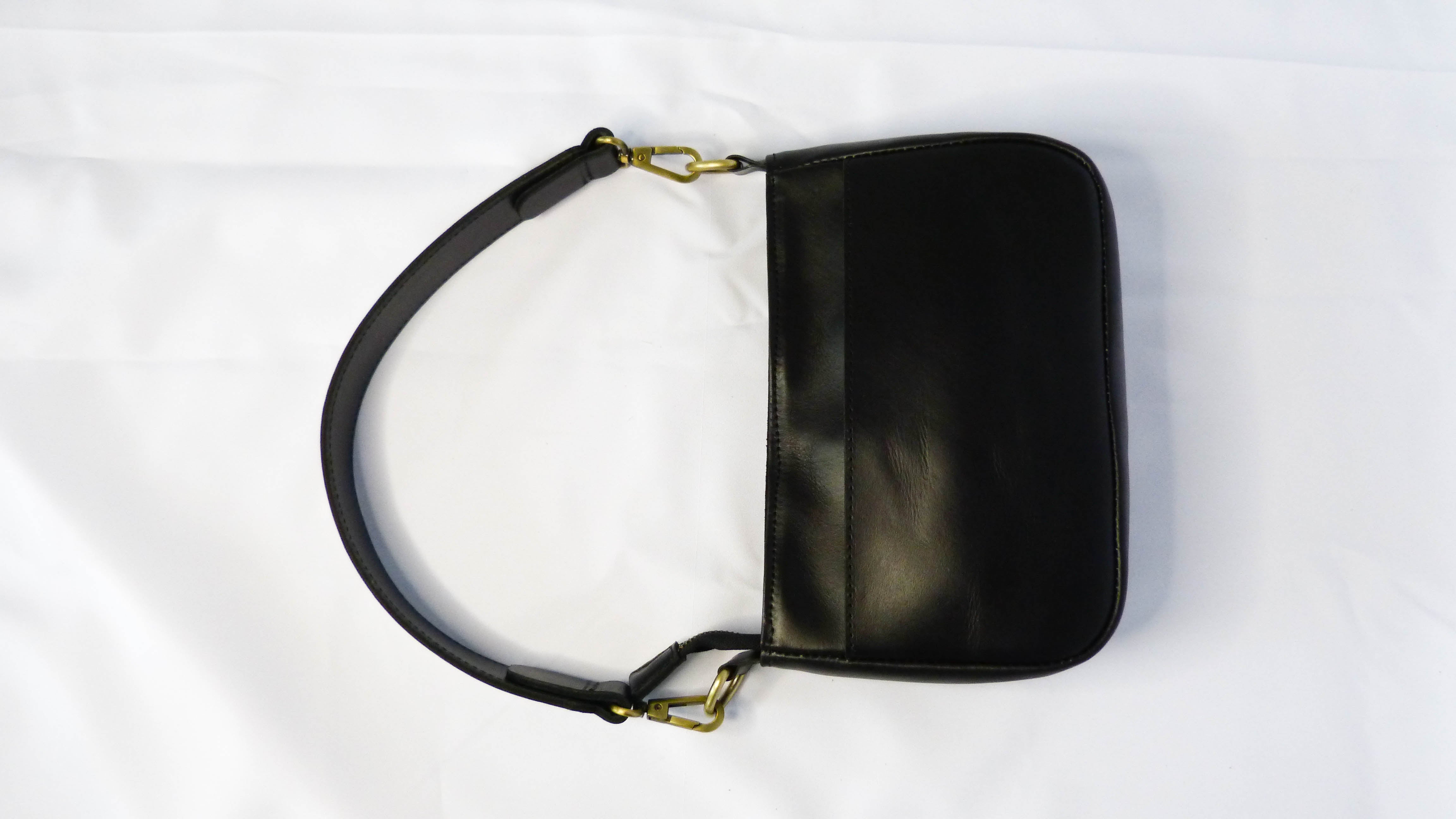 A black leather Jessica purse with gold hardware and chain detail, handmade by Ethiopian artisans. Features a zippered top, inside zipper pocket, and removable shoulder strap for versatile wear.