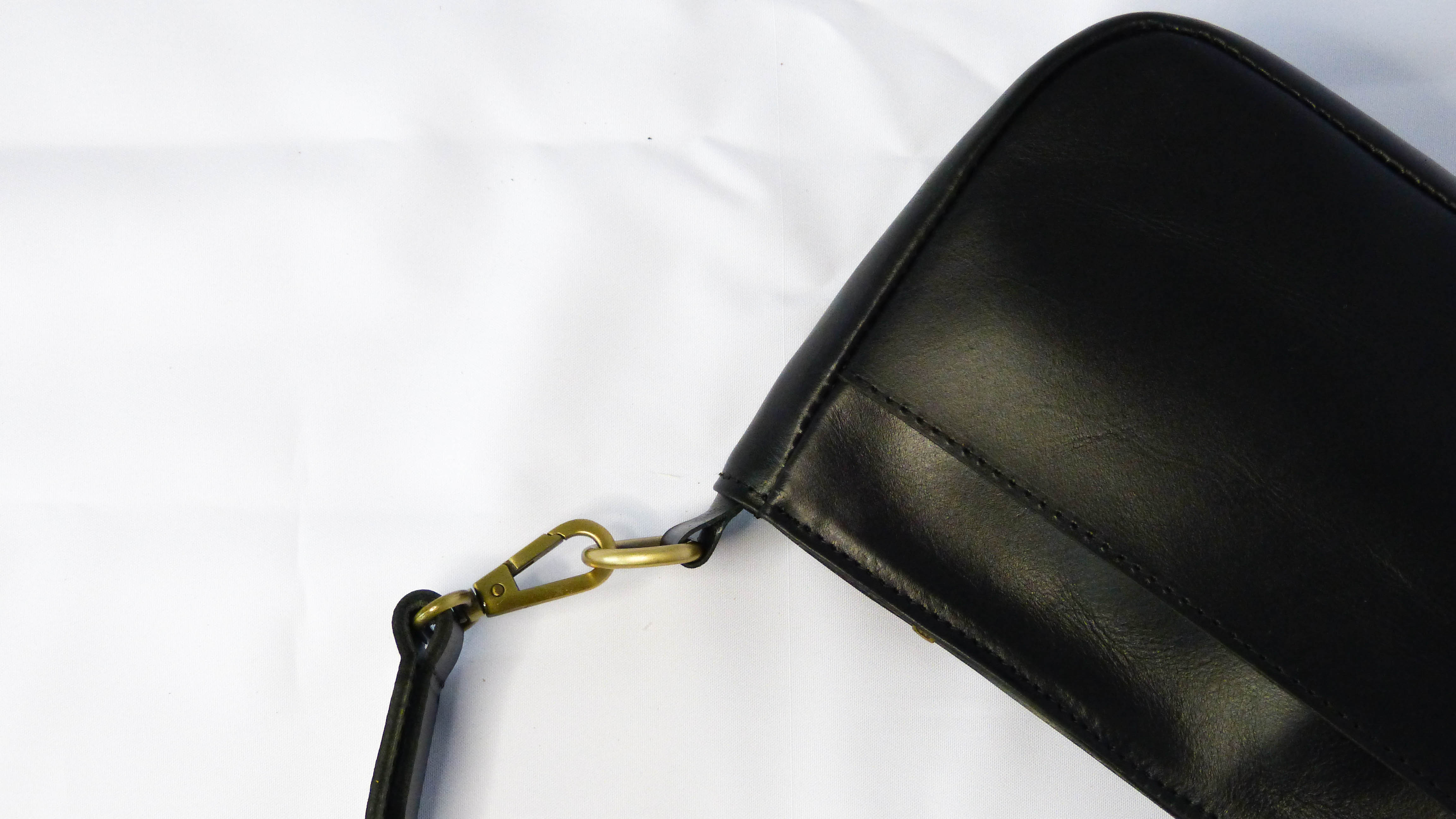 A black leather Jessica purse with a gold hook and clasp, featuring a removable shoulder strap, zippered top, inside and outside pockets. Handmade by Ethiopian artisans.