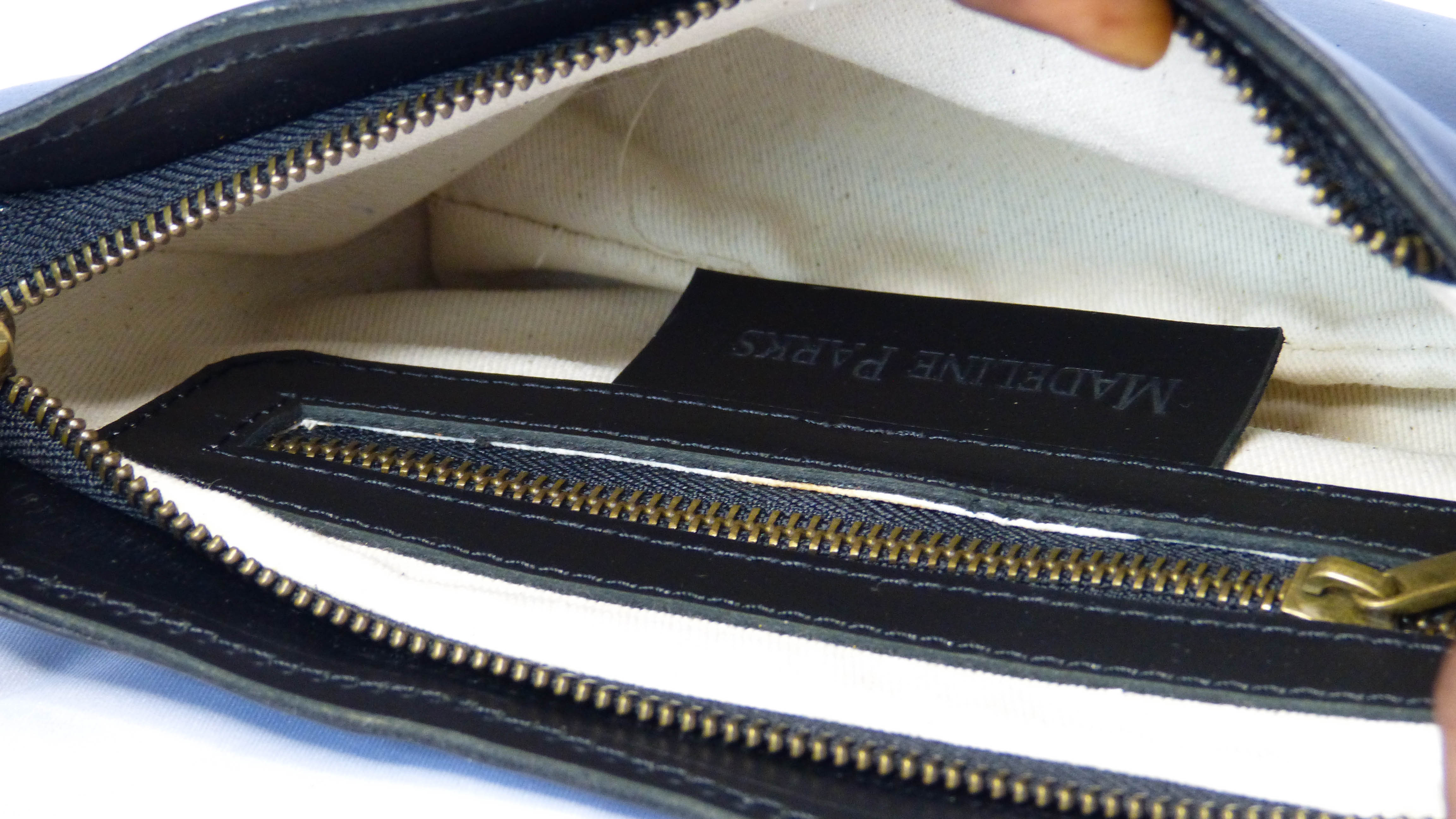 A close-up of a zipper on the Jessica Leather Purse in Black Licorice by Madeline Parks Designs. Handmade in Ethiopia with soft leather, featuring a zippered top, inside pocket, and removable shoulder strap.