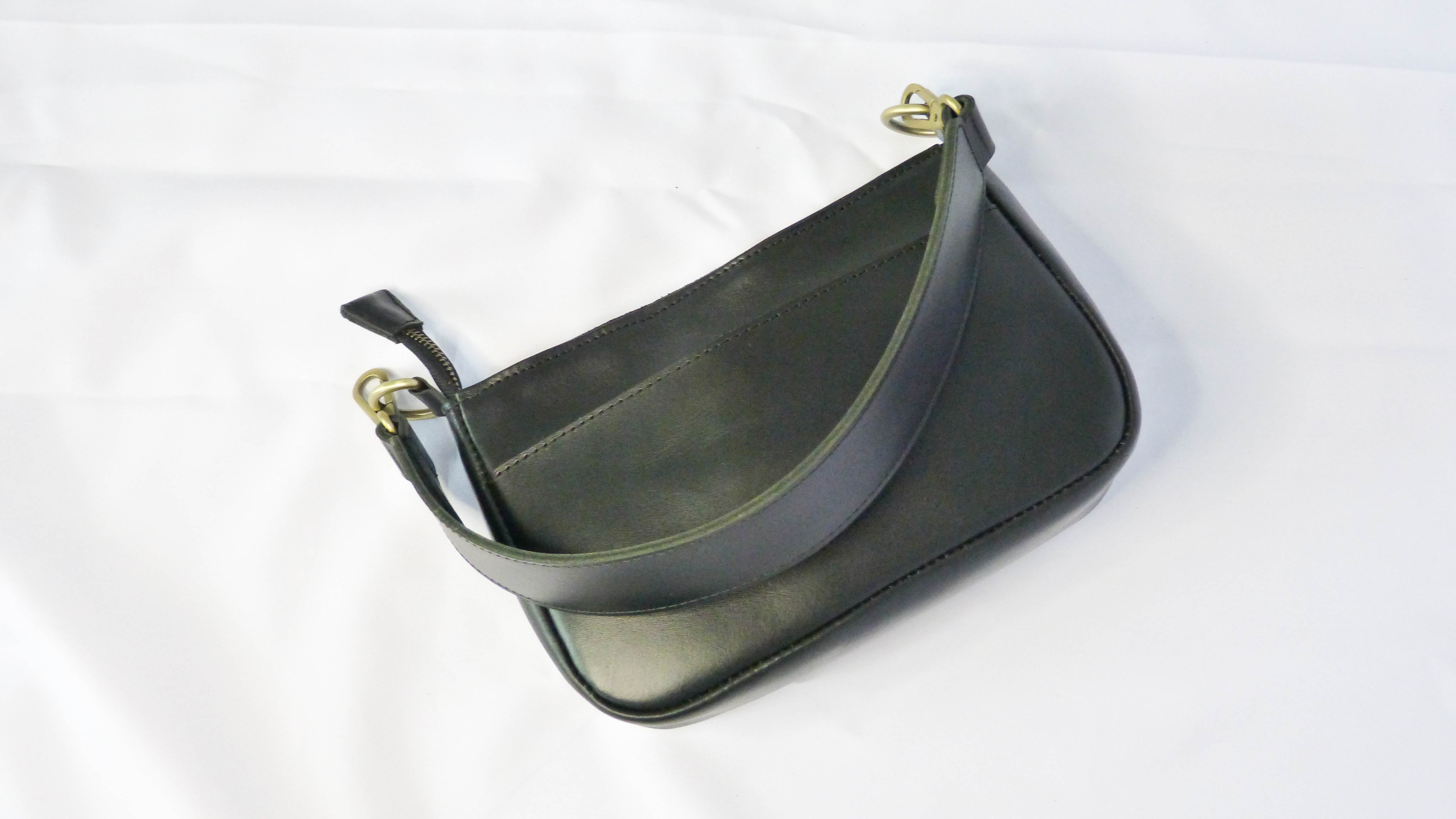 A black leather purse with a removable shoulder strap, zippered top, and inside/outside pockets. Handmade by Ethiopian artisans, measuring 9 x 5.5 x 2.25. Designed by Madeline Parks Designs.