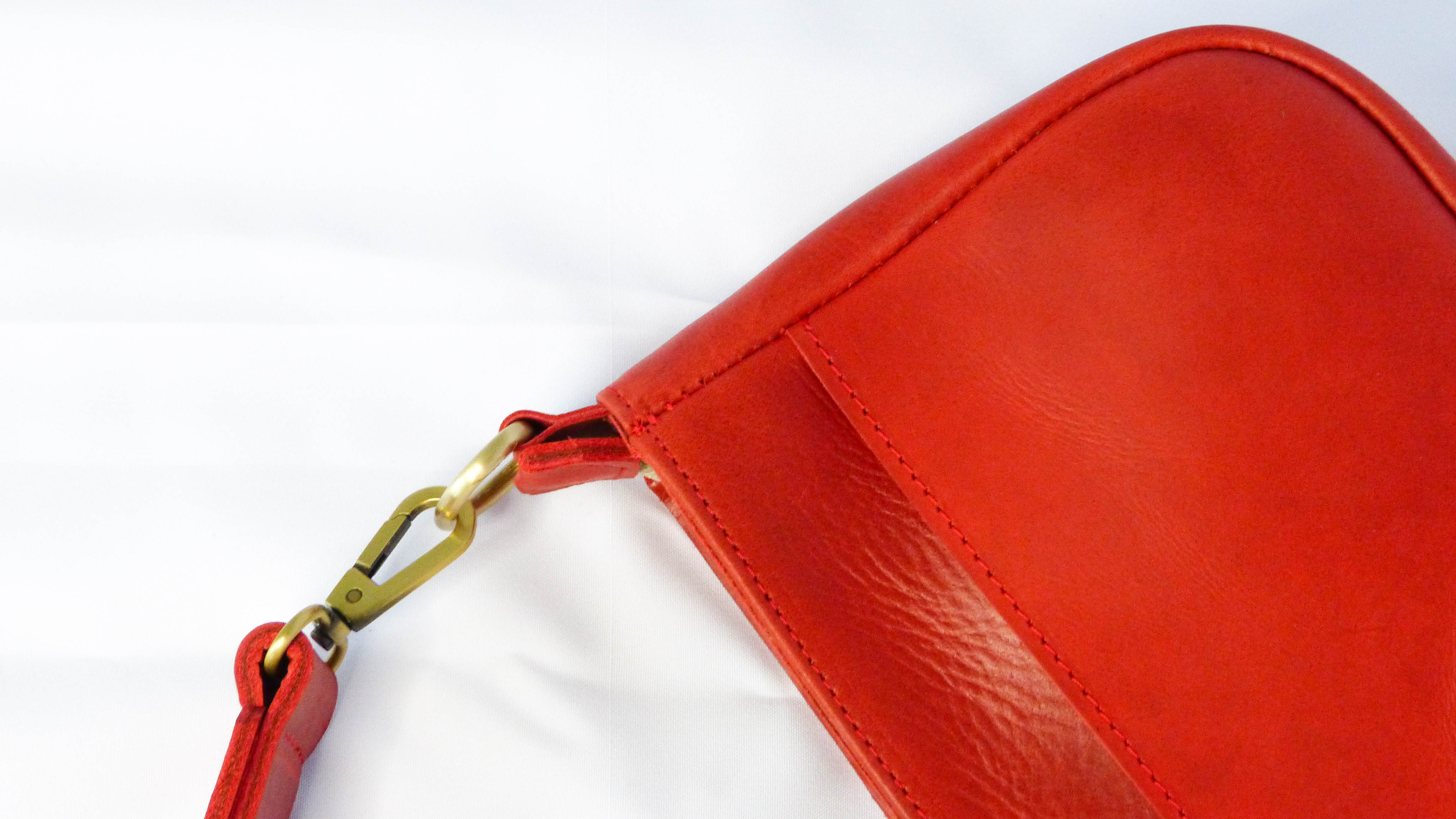 A close-up of the Jessica Leather Purse in Cherry, showcasing red leather with stitching and a removable shoulder strap. Handmade by artisans in Ethiopia, perfect for everyday use.