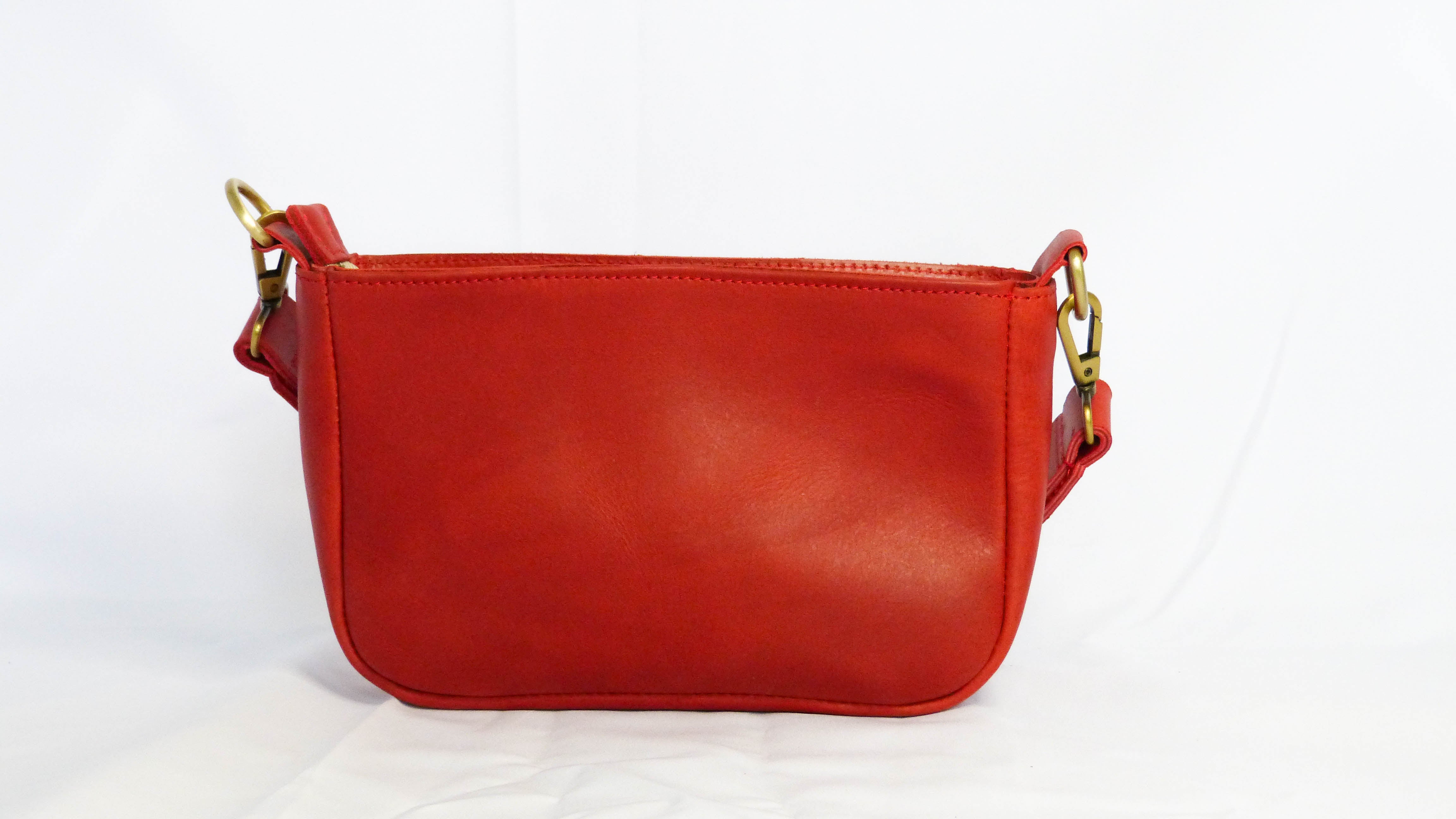 A red leather purse named Jessica, featuring a zippered top, inside zipper pocket, and removable shoulder strap. Handmade by Ethiopian artisans from soft leather. Dimensions: 9 x 5.5 x 2.25.