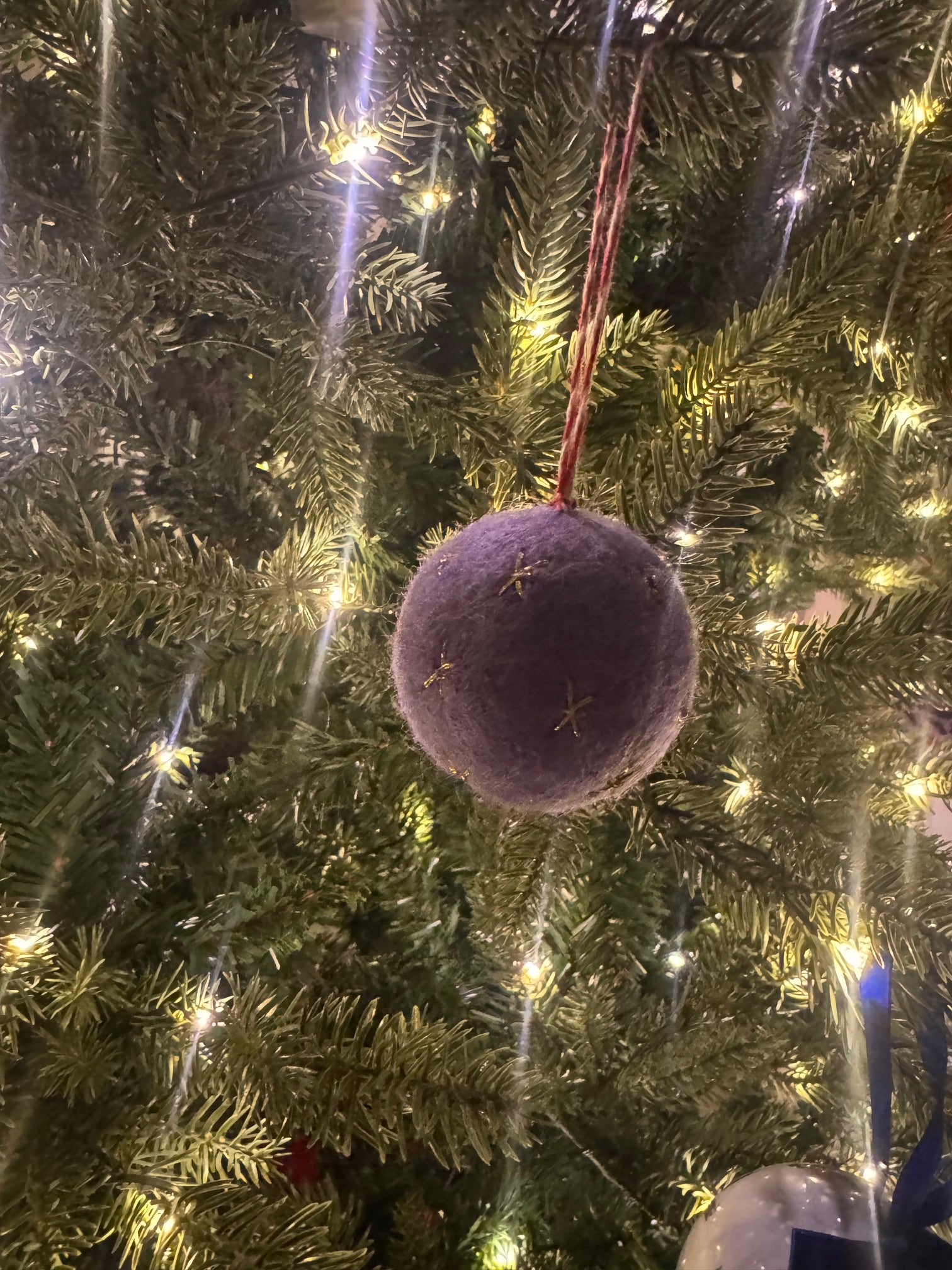 Purple Felt Ornament with gold stars, hanging on a Christmas tree, reflecting Madeline Parks ®'s commitment to artisanal craftsmanship and festive elegance.