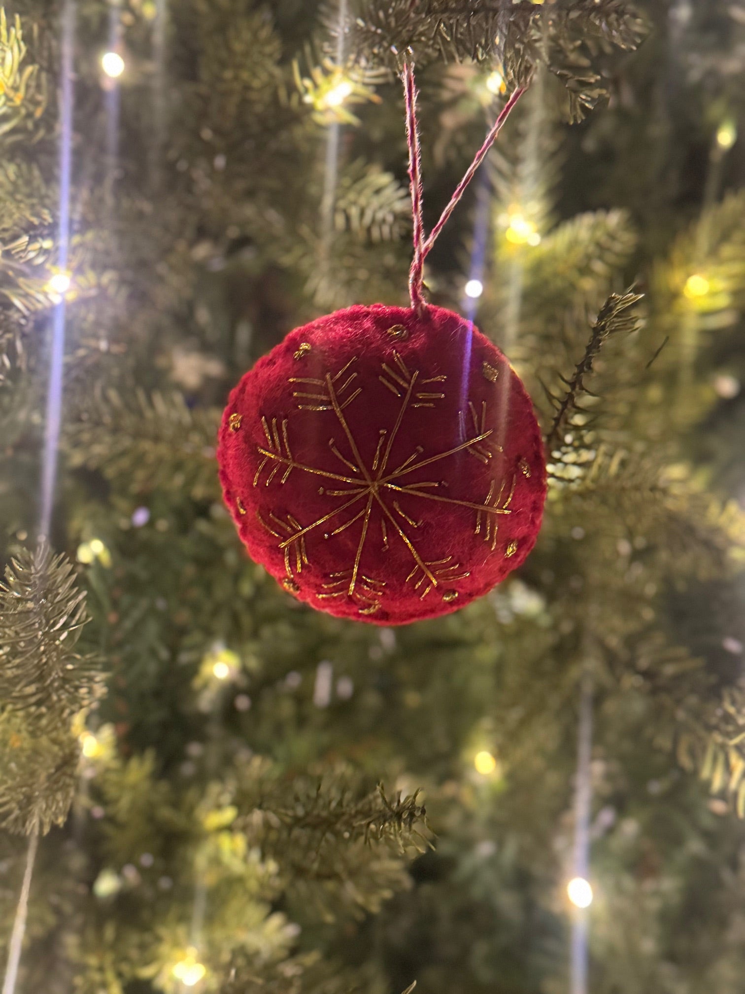 Red Felt Ornament hanging from a Christmas tree, showcasing intricate craftsmanship, fitting the artisan aesthetic of Madeline Parks ®'s holiday collection.