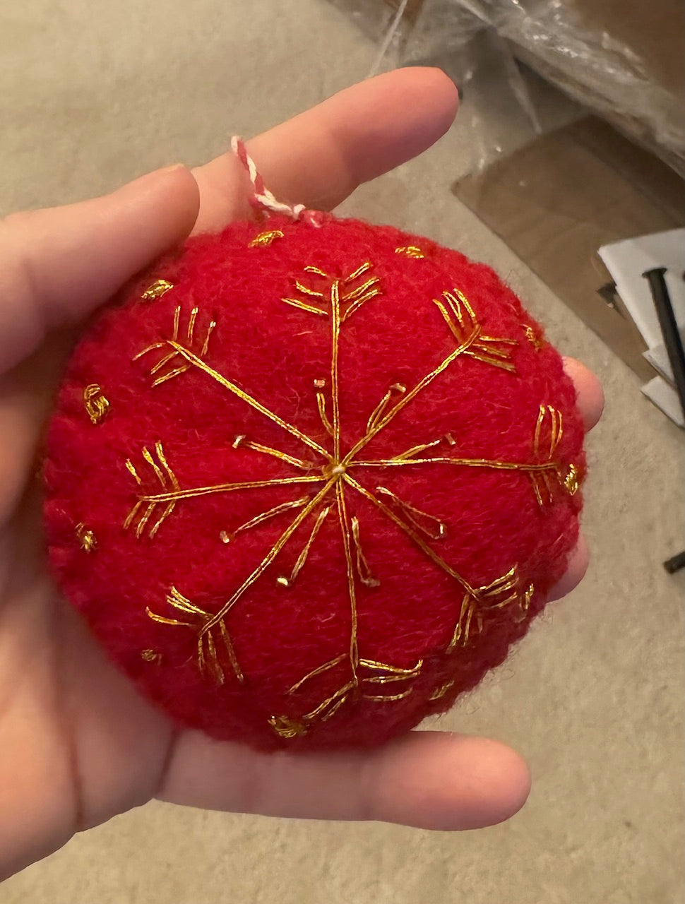 Hand holding a Red Felt Ornament with gold snowflake detailing, showcasing Madeline Parks ™'s commitment to artisan craftsmanship and intricate design.