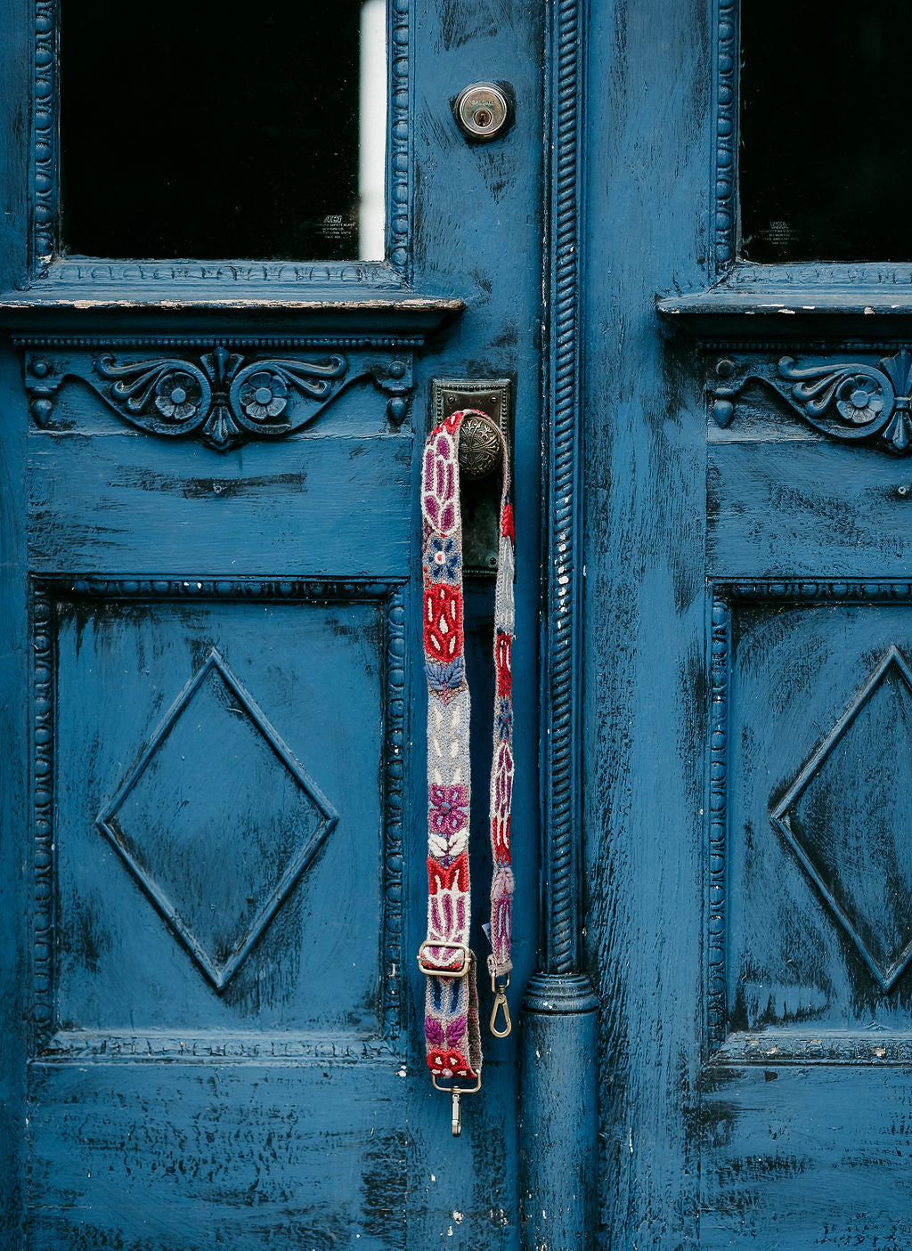 the Purple Adjustable Purse Strap displayed on a blue antique door.