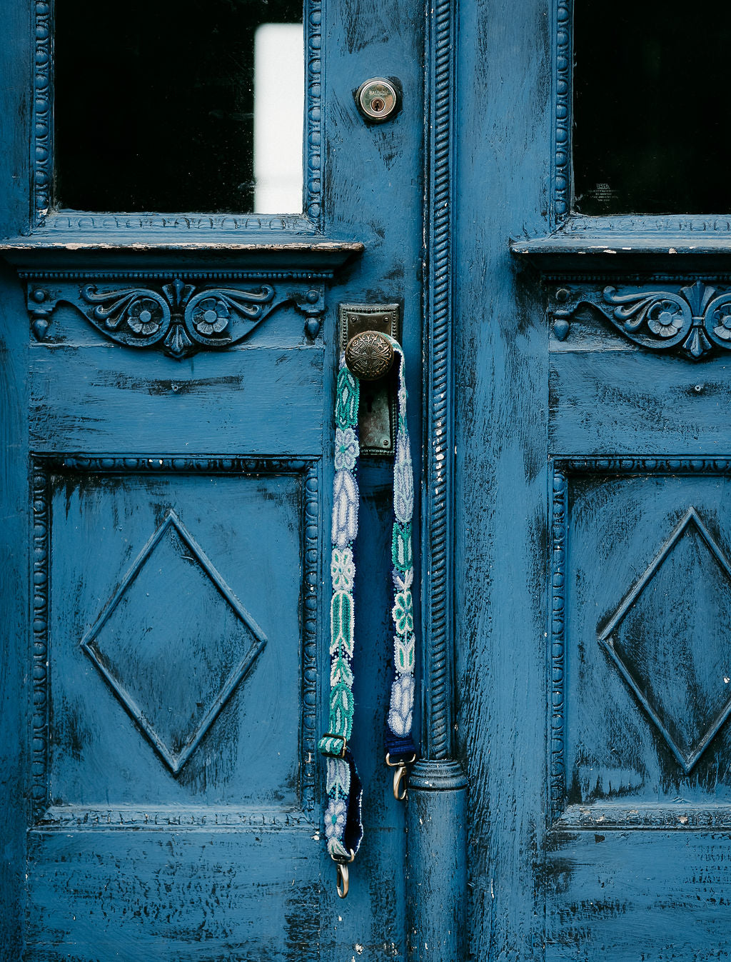 Blues Adjustable Strap displayed hanging from the doorknob of an antique blue door.