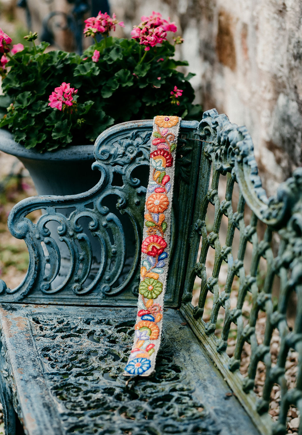 Fair Trade handmade purse strap in colorful floral design displayed on a bench in outdoor setting.