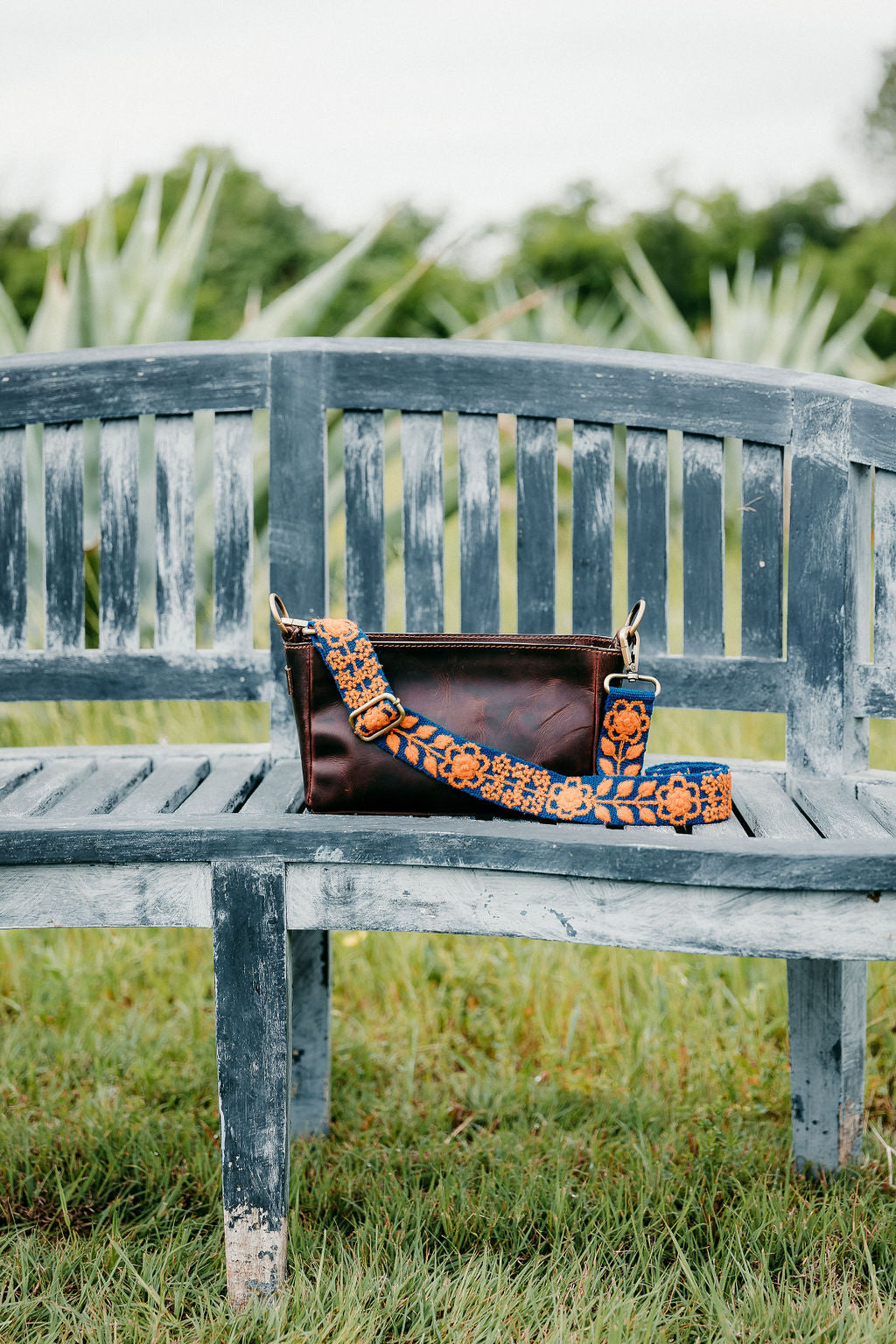 Kenley Adjustable Strap attached to brown leather purse displayed on a bench
