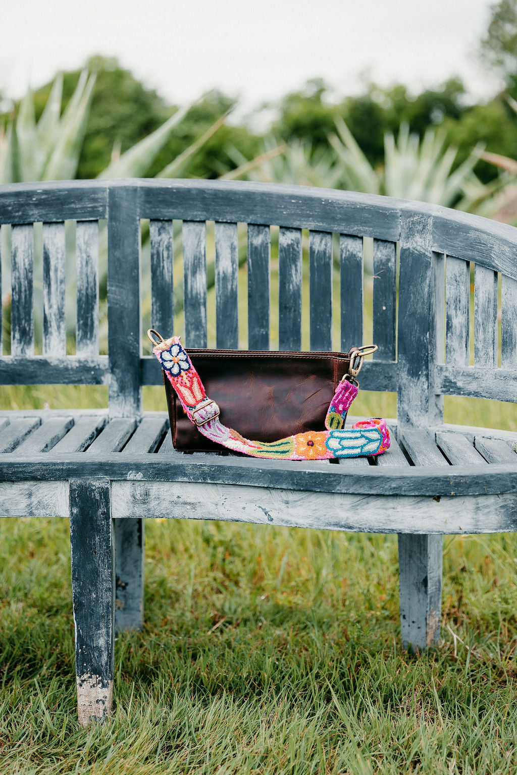 Hot Pink Adjustable Strap purse attached to brown leather fair trade purse displayed outside on a benc