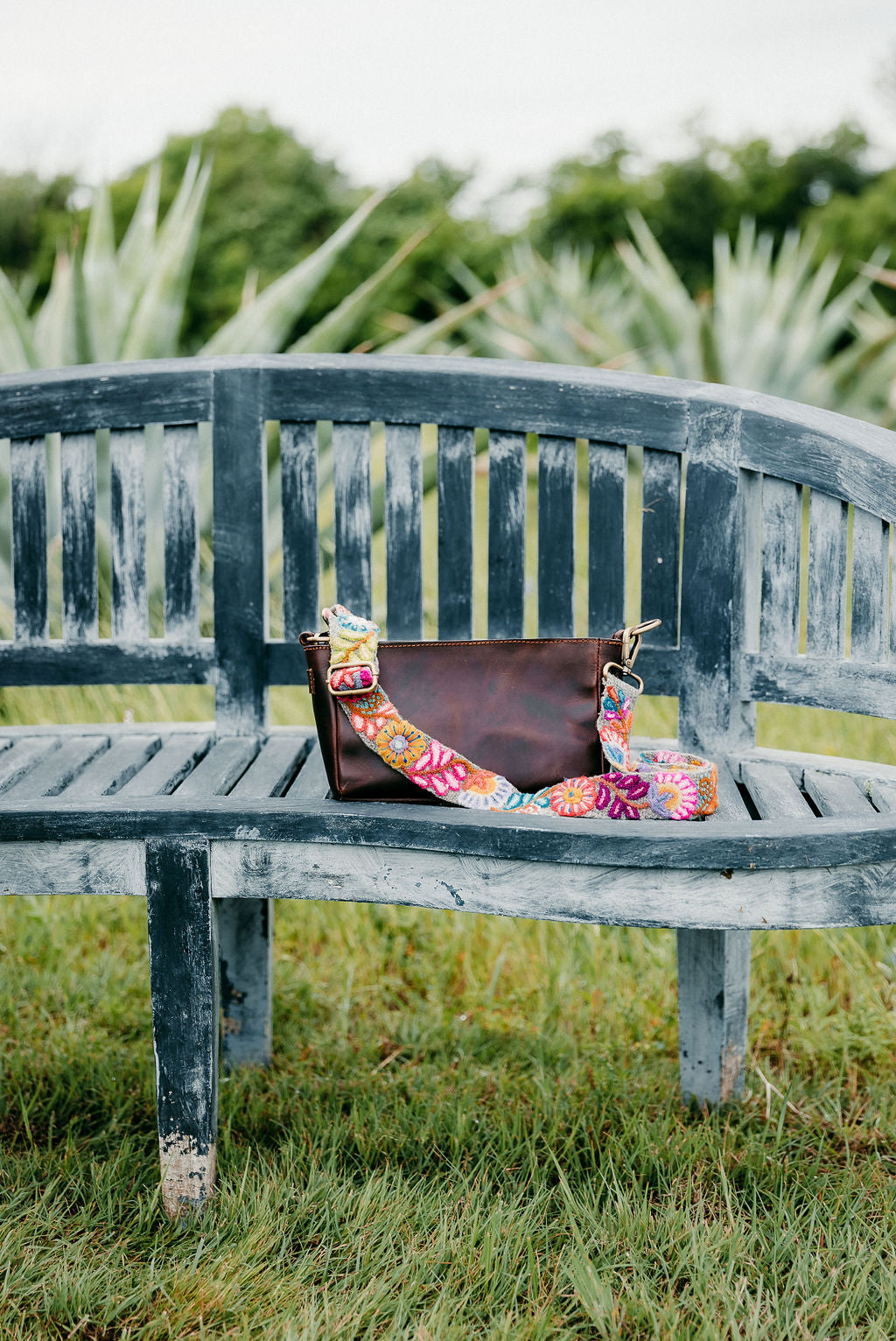 Bright Adjustable Purse Strap attached to brown leather purse displayed on a bench in an outdoor setting.