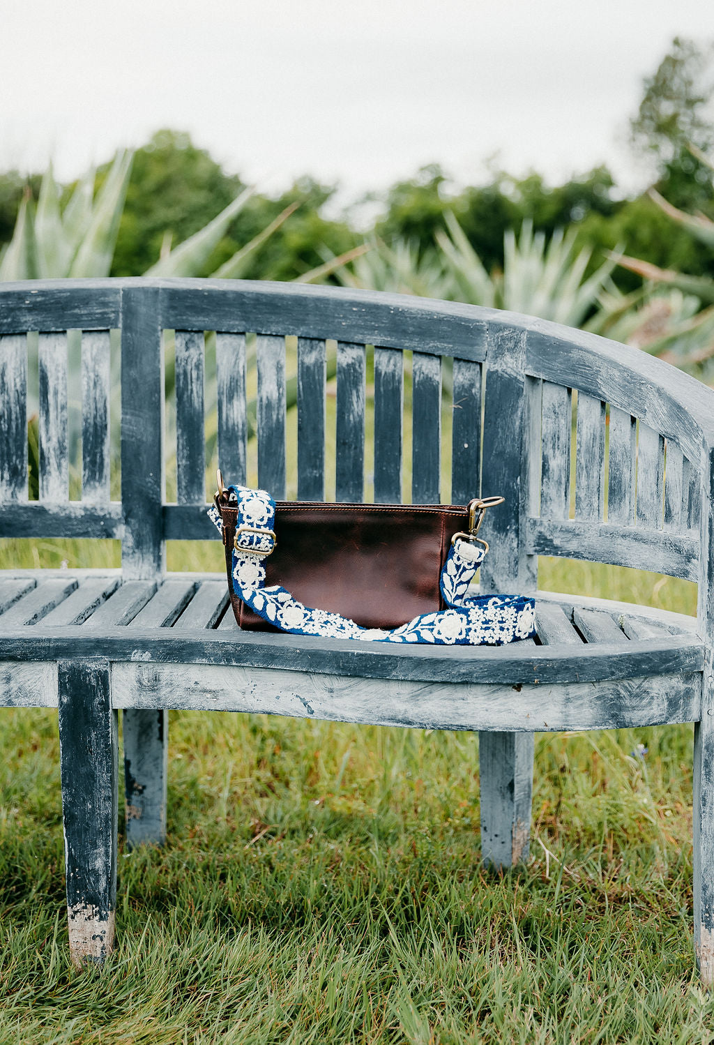 Tess Adjustable Strap attached to brown leather purse displayed on a blue bench.
