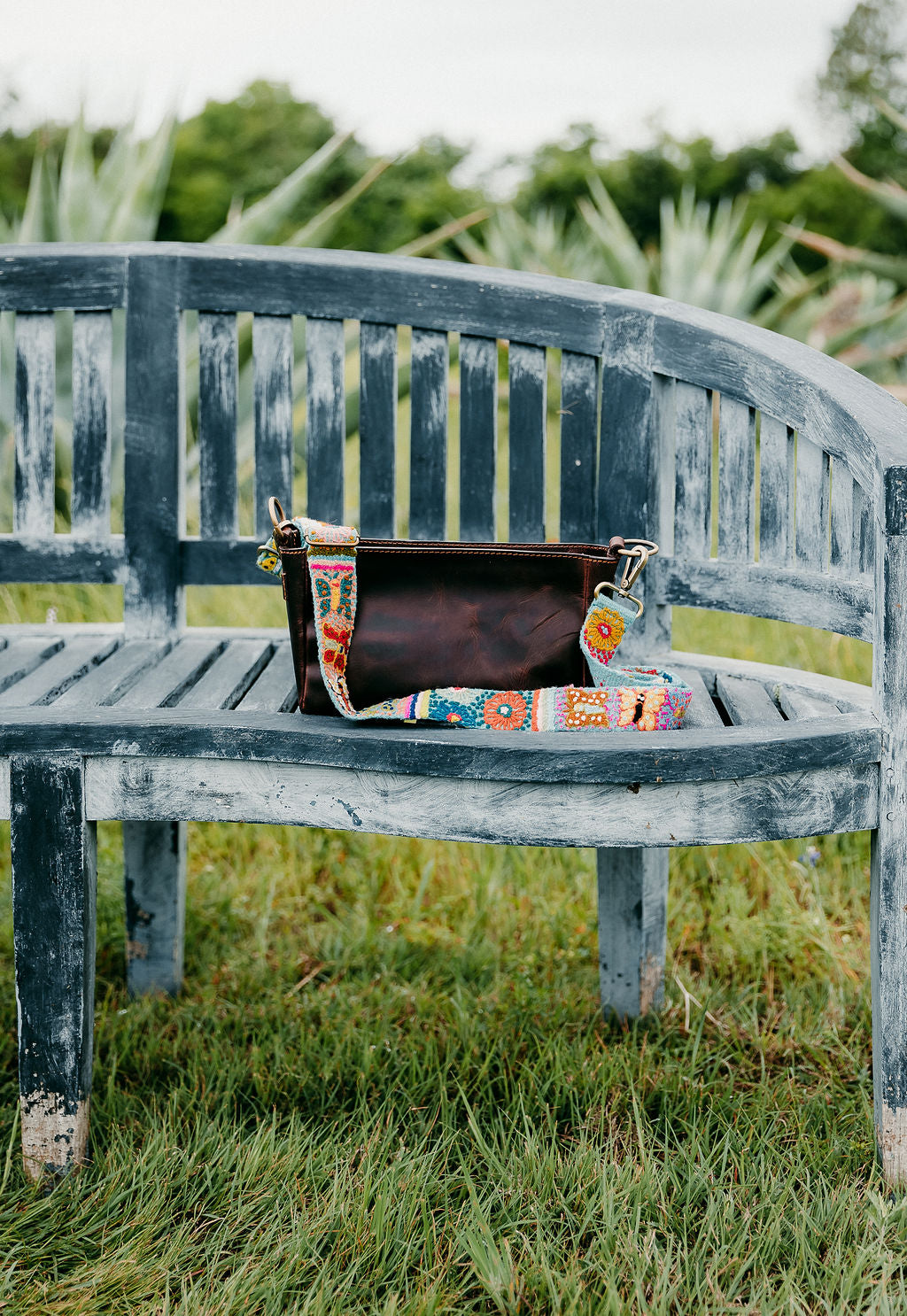 Butterfly Adjustable Strap attached to a brown leather purse displayed on Bench.