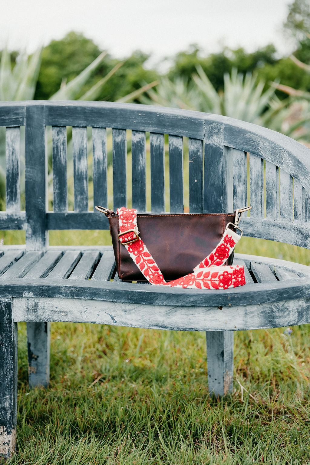 Abbey Adjustable Strap attached to brown leather purse displayed on a bench in the outdoors.