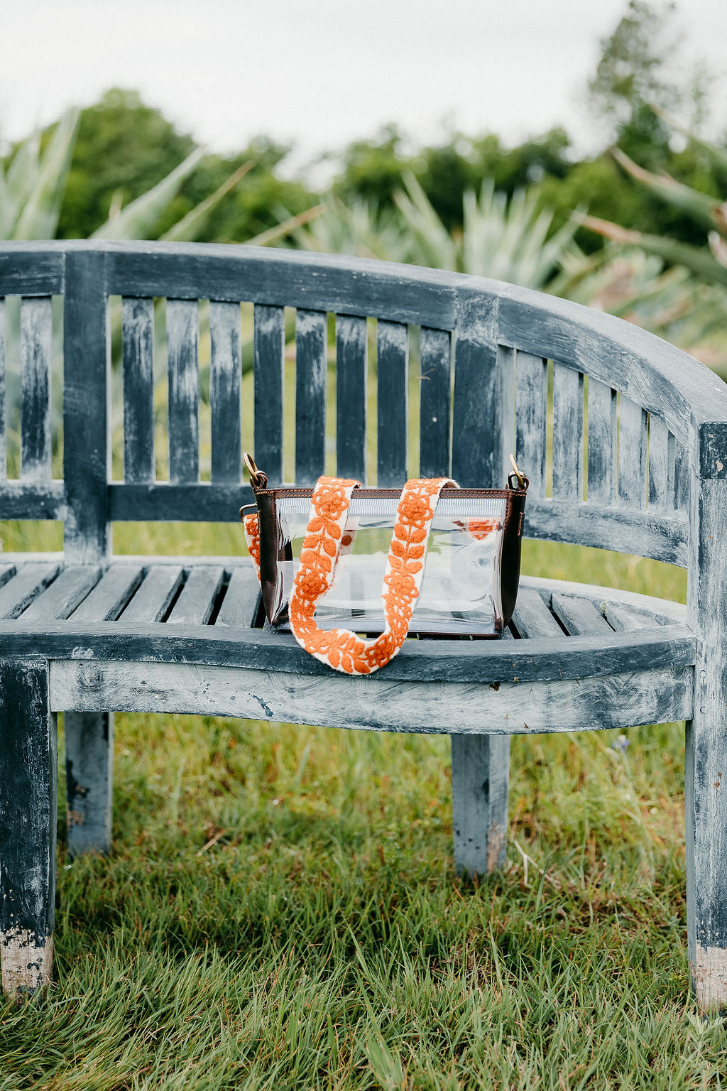 Rachel Adjustable Strap attached to  clear bag on a bench in the grass.