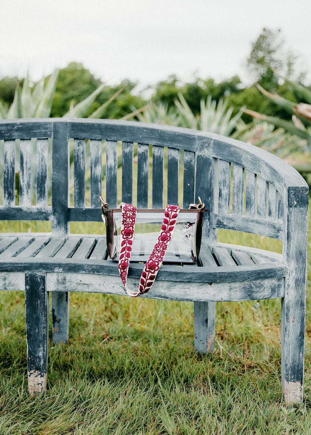 Jen Clear Purse on a bench with a bag and a flower embroidery.