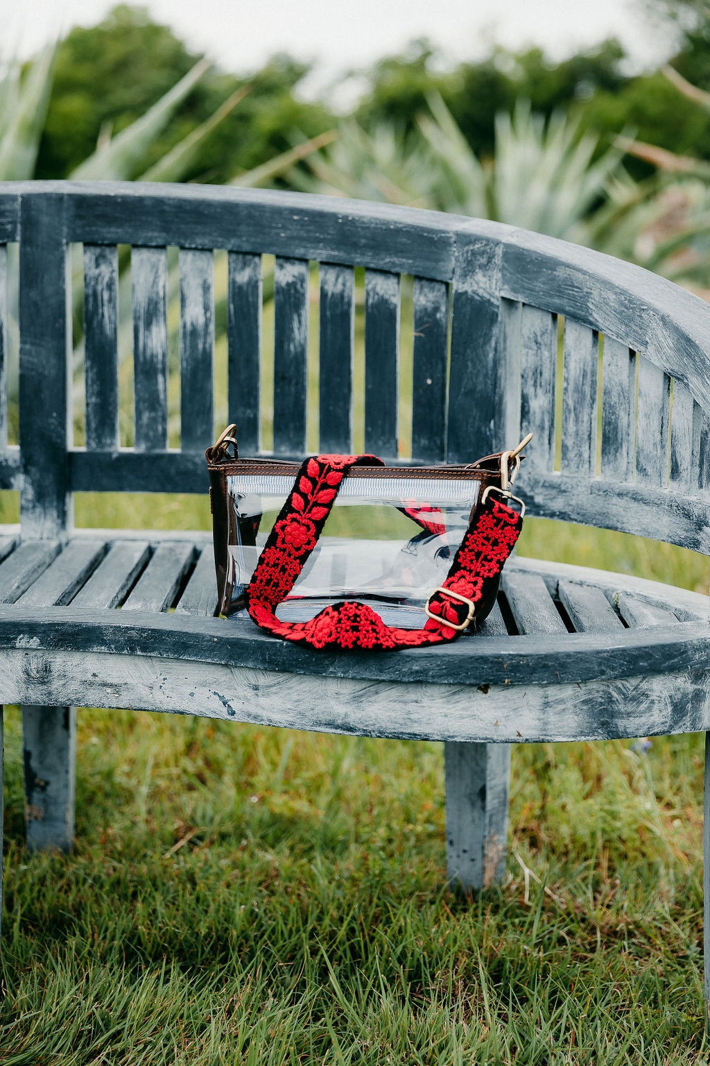 Kennedi Adjustable Strap attached to a leather clear purse shown on a bench.