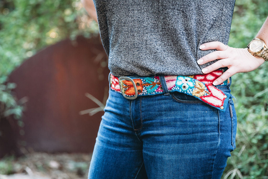 A person wearing a colorful belt with a navy floral embroidered design from Madeline Parks Designs.