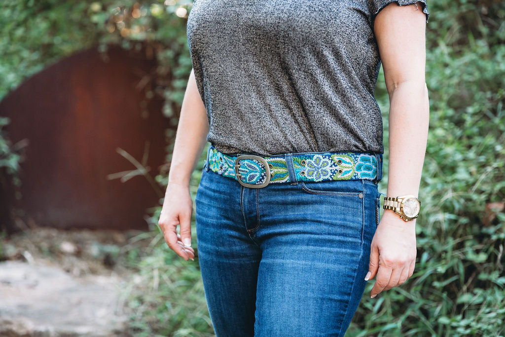 A woman wearing a grey shirt and blue jeans, showcasing the Blues Embroidered Belt from Madeline Parks.