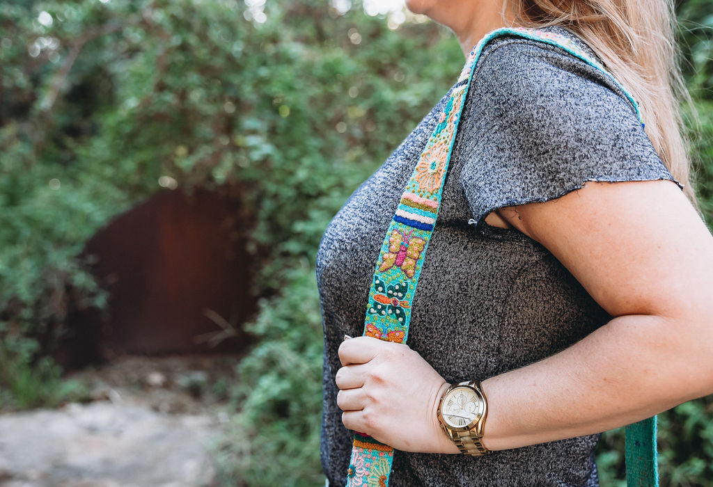 A woman holding a butterfly adjustable purse strap, hand embroidered by Fair Trade artisans in Peru.