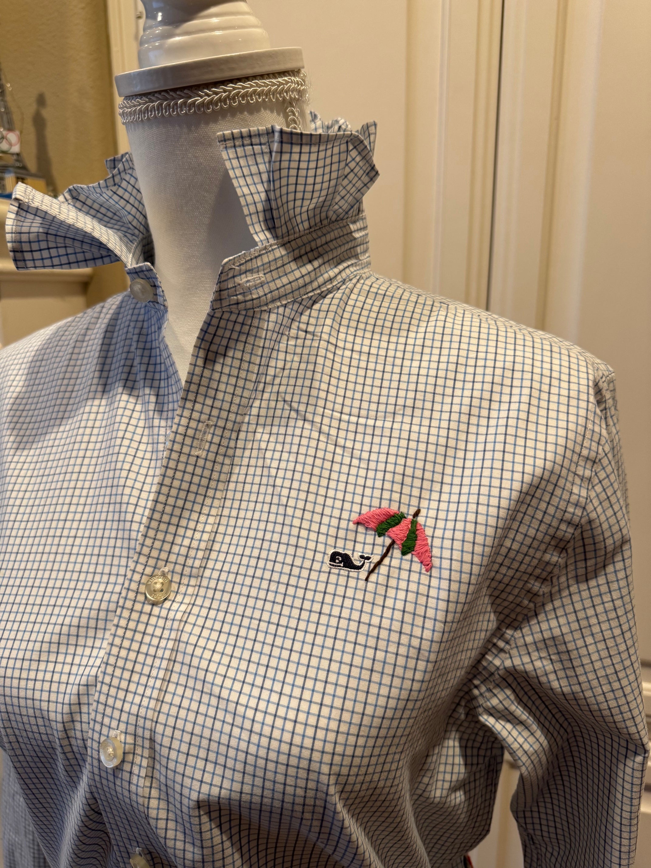 A men's long-sleeve button-up shirt with a blue and white gingham pattern and a pink embroidered umbrella motif on the chest, displayed on a white mannequin torso.