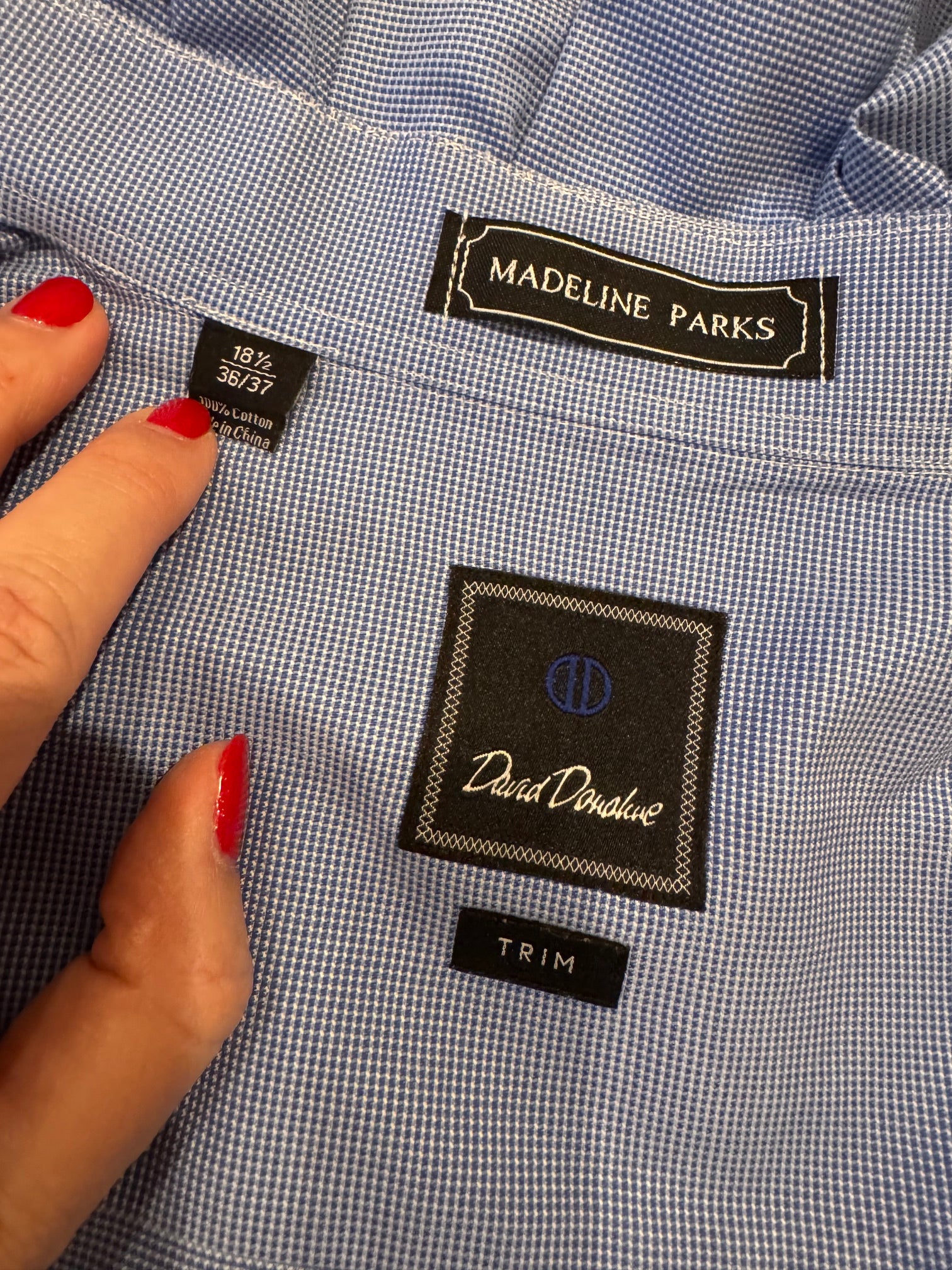 Close-up of a blue and white micro-check dress shirt showing the inner neck labels, including a Madeline Parks label and a David Denman label, with a hand adjusting the collar.