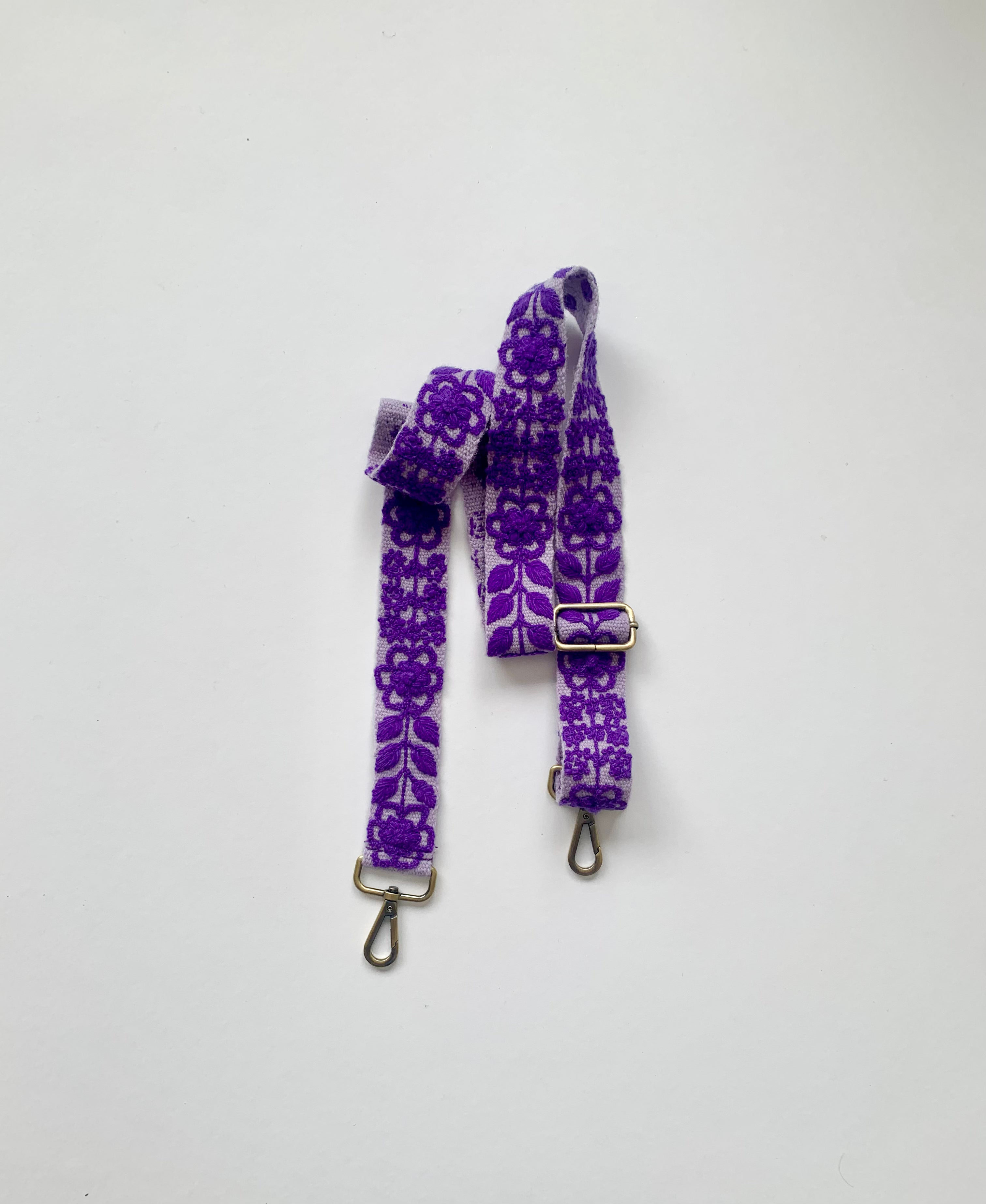 Eliza Adjustable Purse Strap, a purple strap with metal clasps and a floral design. 