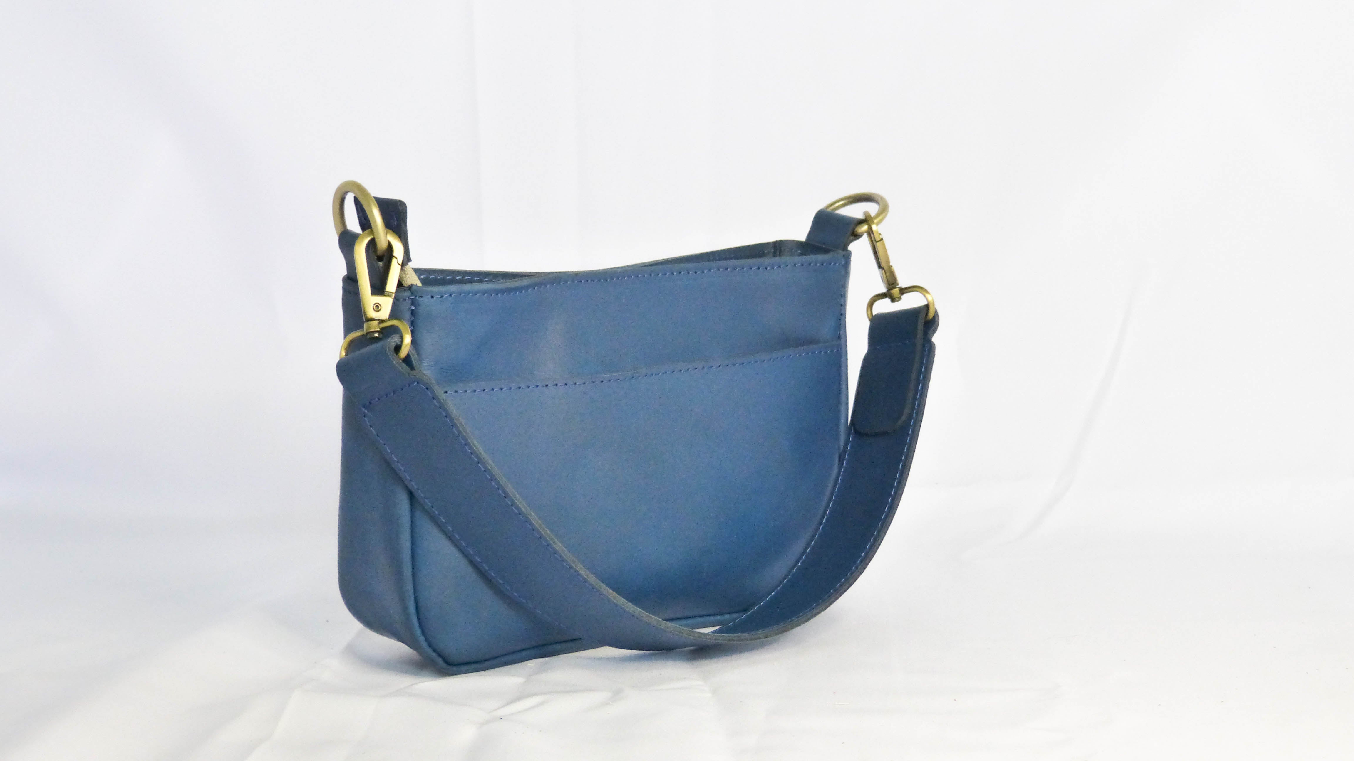 A blue leather Jessica purse with gold handles, removable shoulder strap, zippered top, inside pocket, and outside phone pocket. Handmade by Ethiopian artisans for Madeline Parks Designs.
