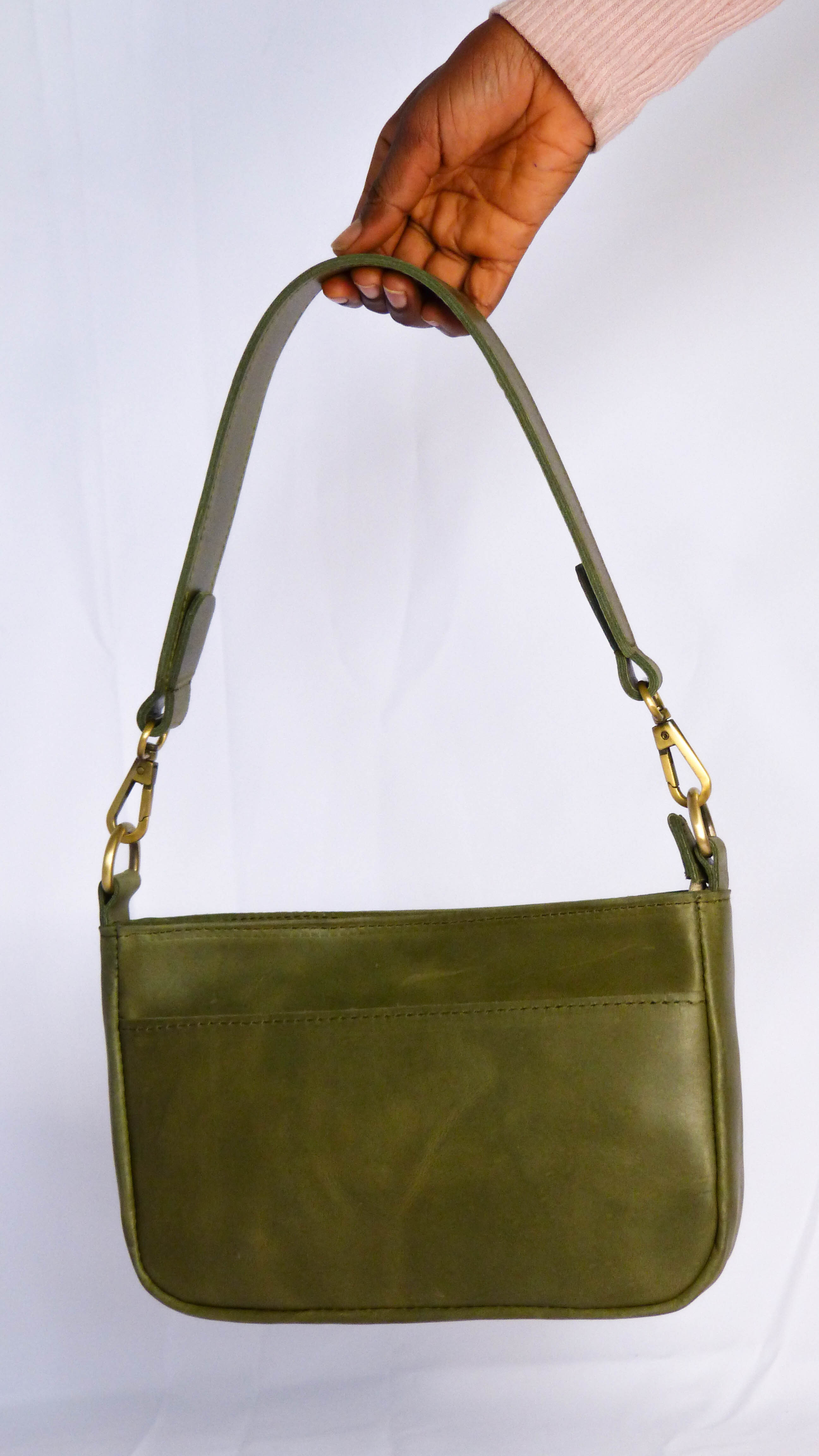 A hand holding the Jessica Leather Purse in Olive, featuring a removable shoulder strap, zippered top, inside zipper pocket, and outside phone pocket. Handmade by Ethiopian artisans.