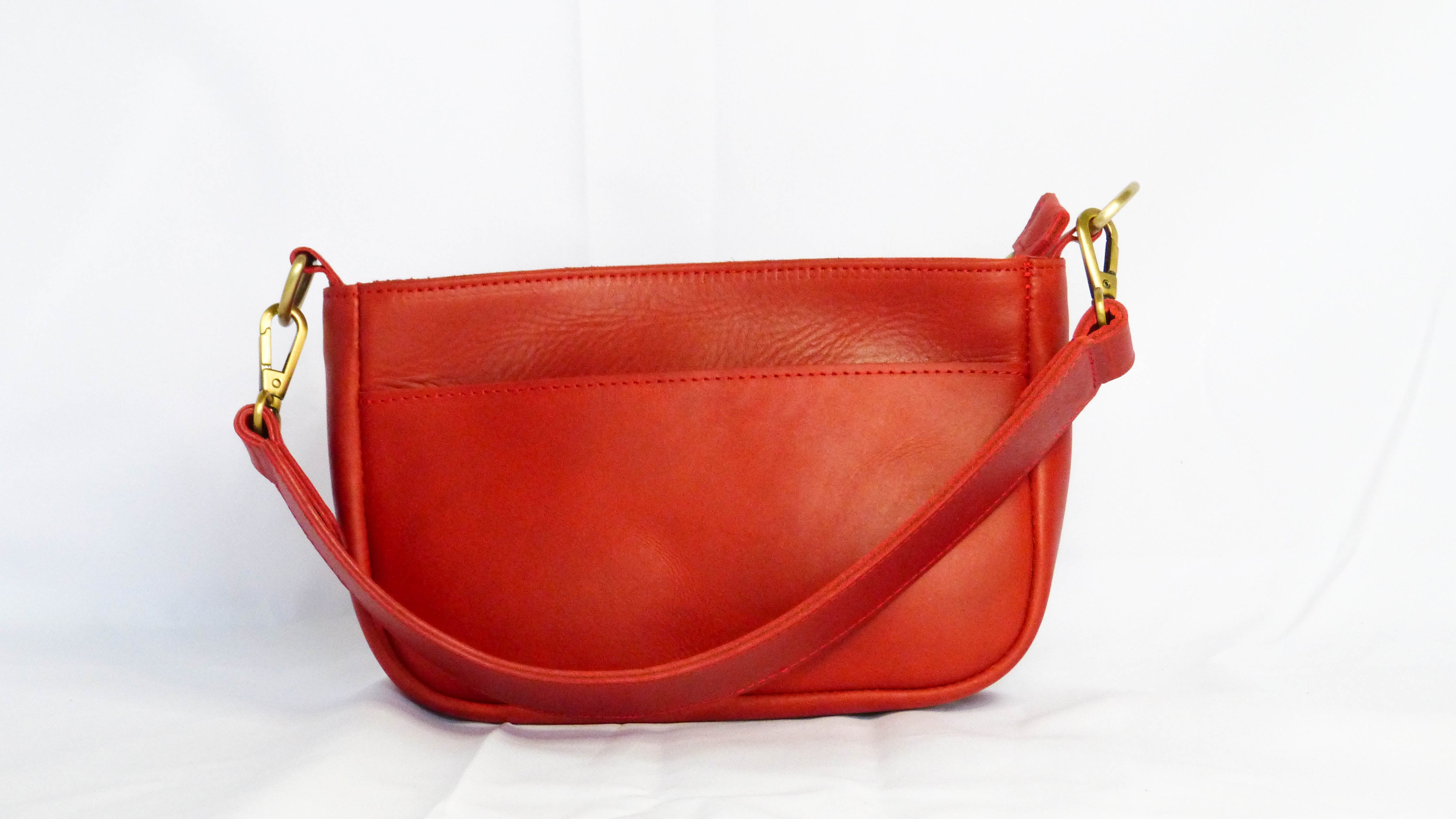 A red leather Jessica purse with removable shoulder strap, zippered top, inside pocket, and outside phone pocket. Handmade by Ethiopian artisans for Madeline Parks Designs.