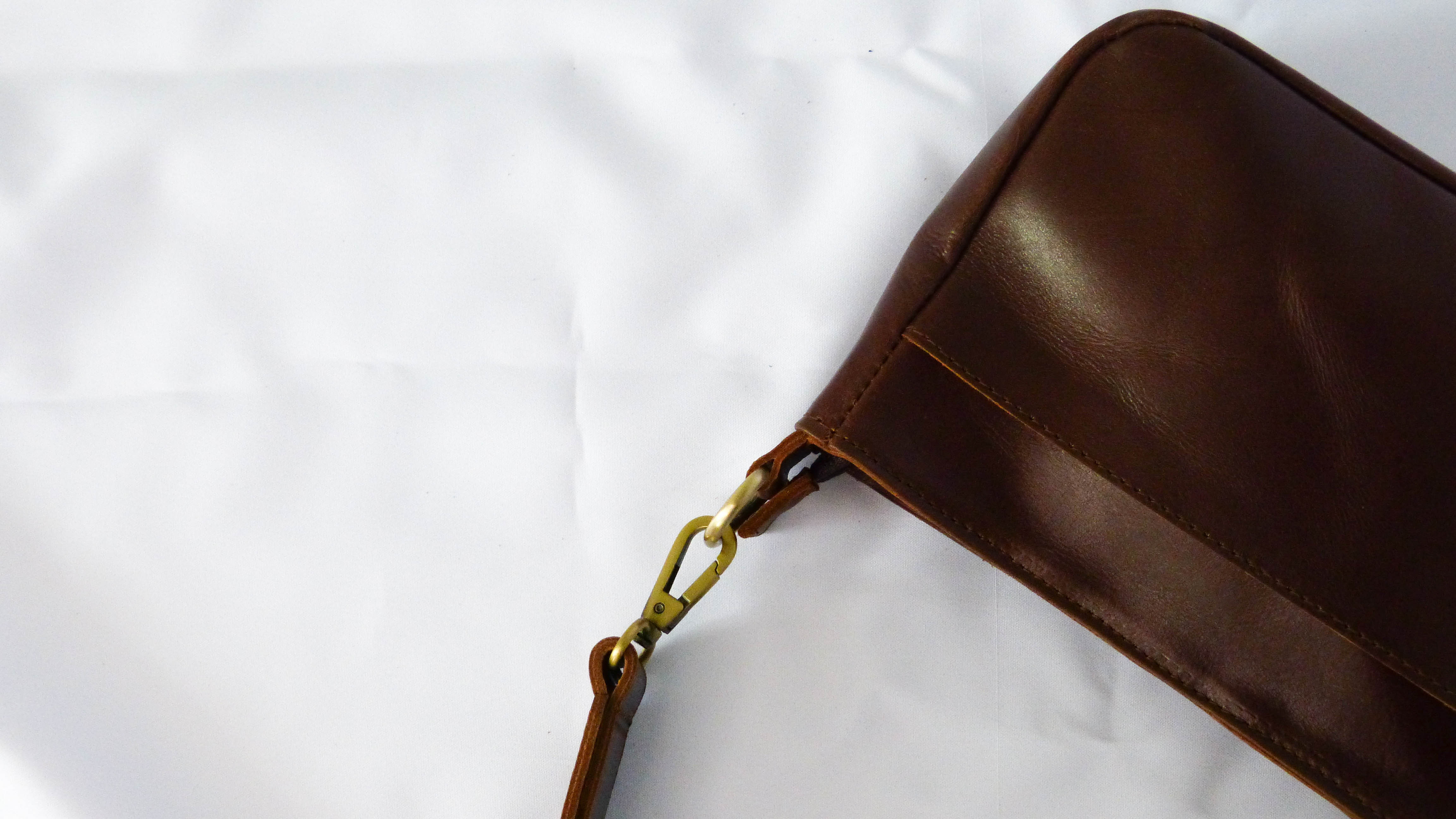 A brown leather purse with a gold clasp and removable shoulder strap. Features zippered top, inside zipper pocket, and outside phone pocket. Handmade by Ethiopian artisans for Madeline Parks Designs.