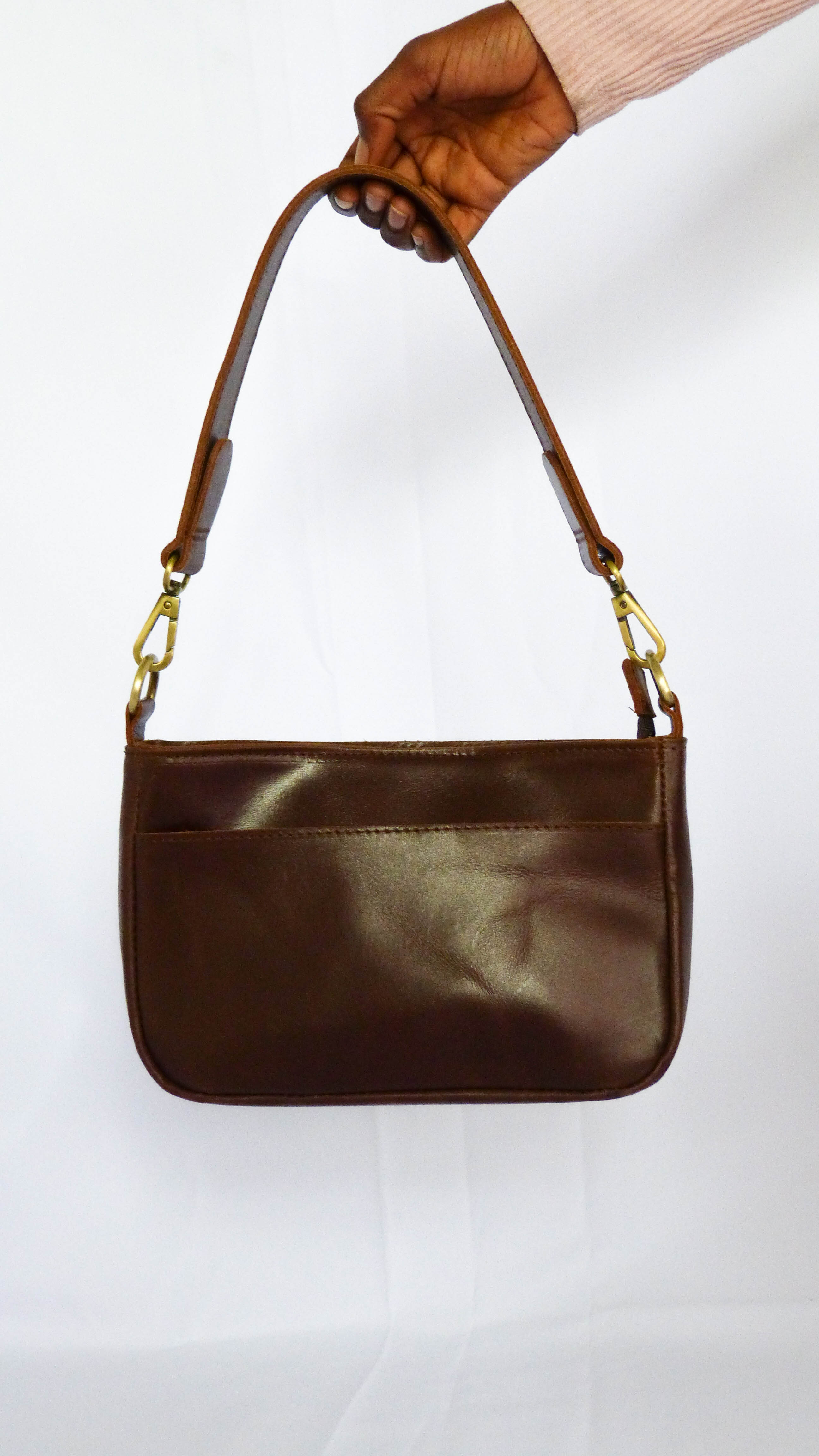 A brown leather purse with gold handles and accents, featuring a removable shoulder strap. Perfect for everyday use, with zippered top, inside zipper pocket, and phone pocket. Handmade by Ethiopian artisans.