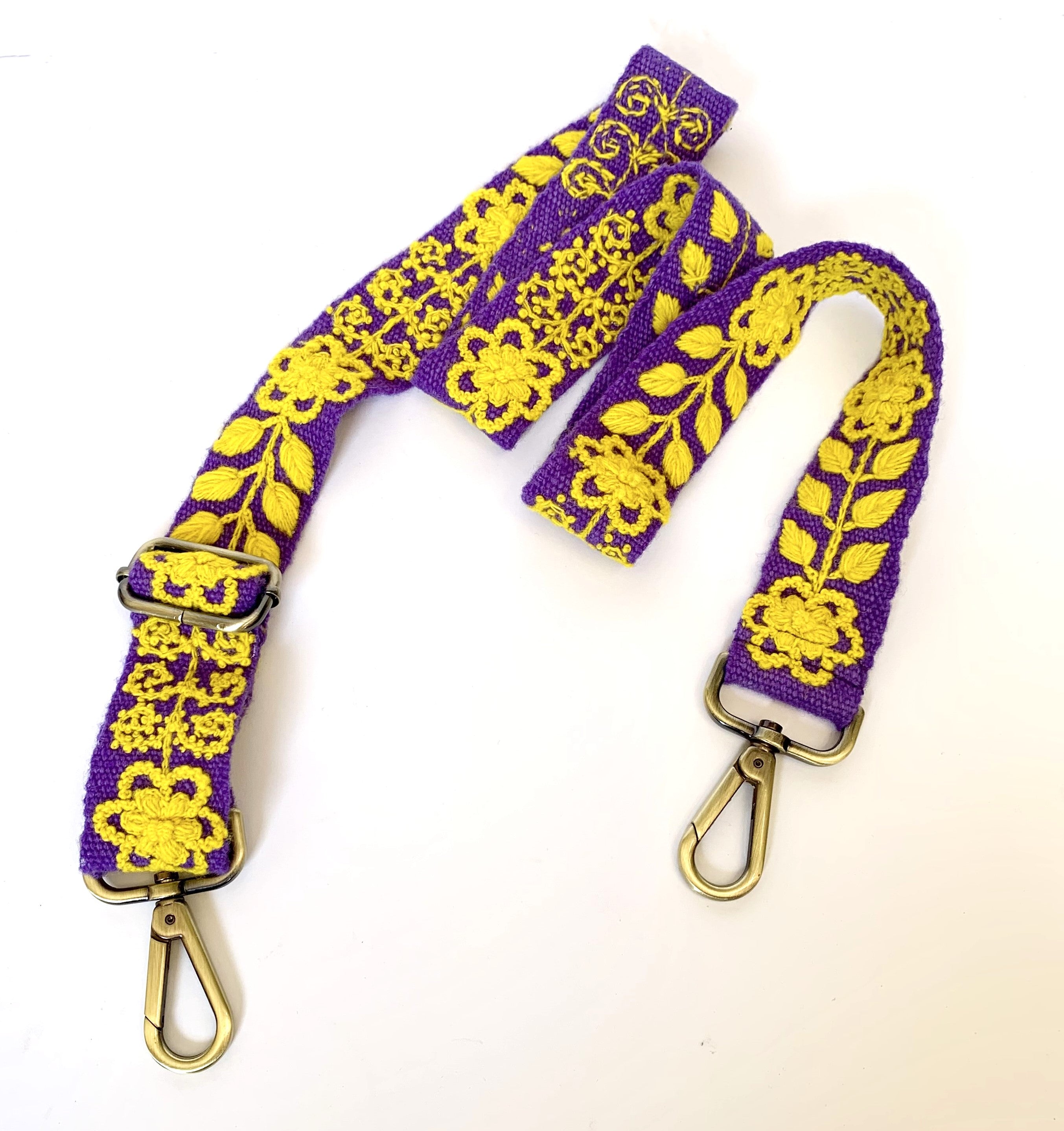 Purple and gold adjustable strap with hand-woven fabric, featuring a gold floral and leaves design. Hand-embroidered by Fair Trade artisans in Peru. Perfect for game day or a night out.