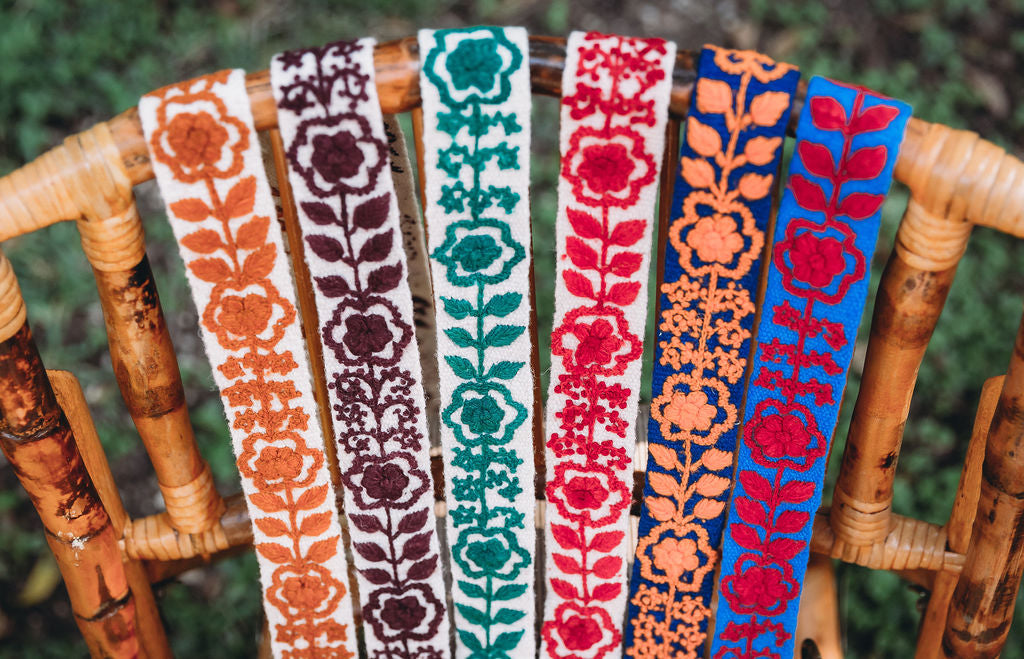 A display of floral school spirit purse straps displayed on the back of a wood chair.