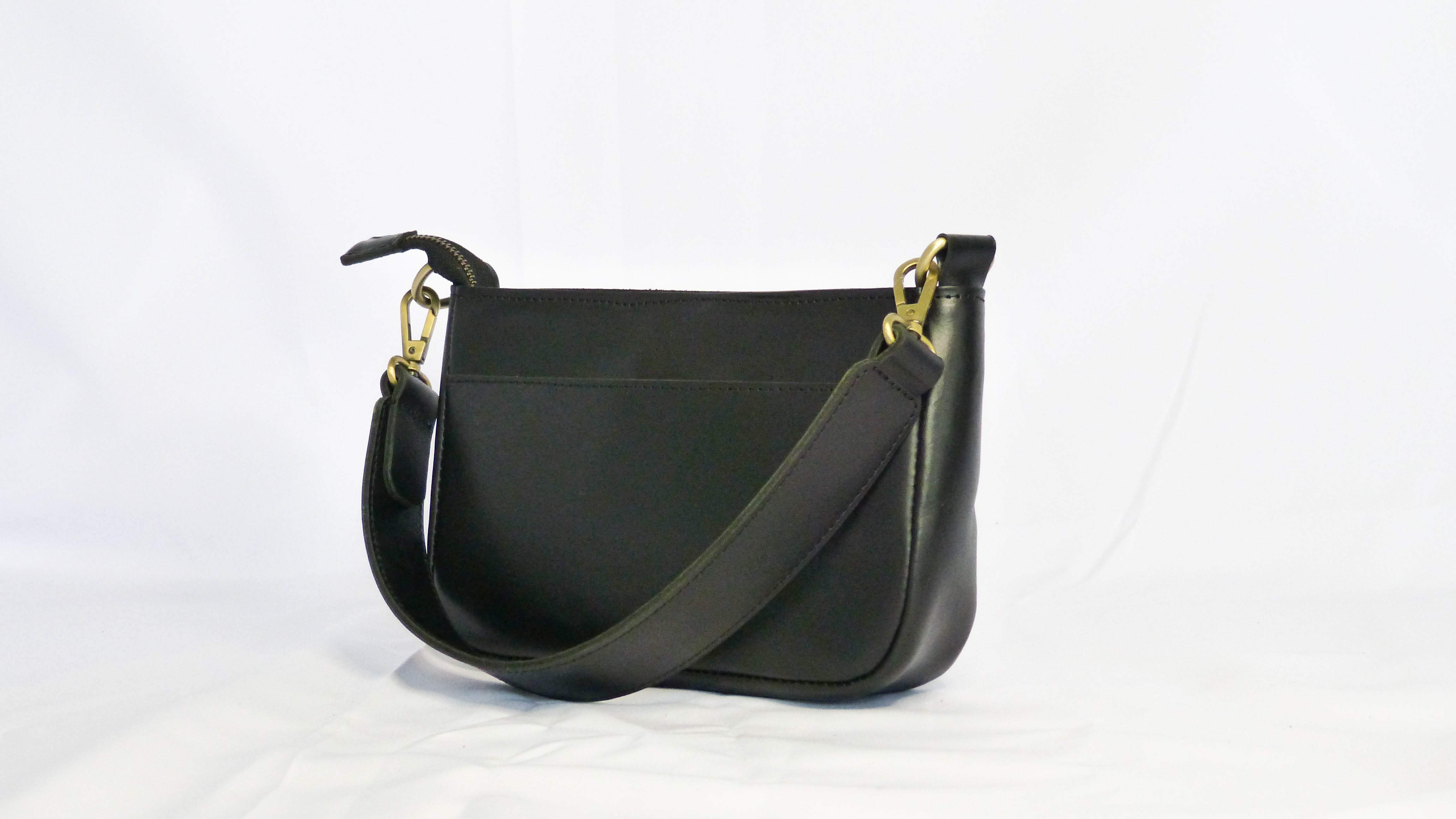 A black leather Jessica purse with a removable shoulder strap, zippered top, inside pocket, and outside phone pocket. Handmade by Ethiopian artisans for Madeline Parks Designs.