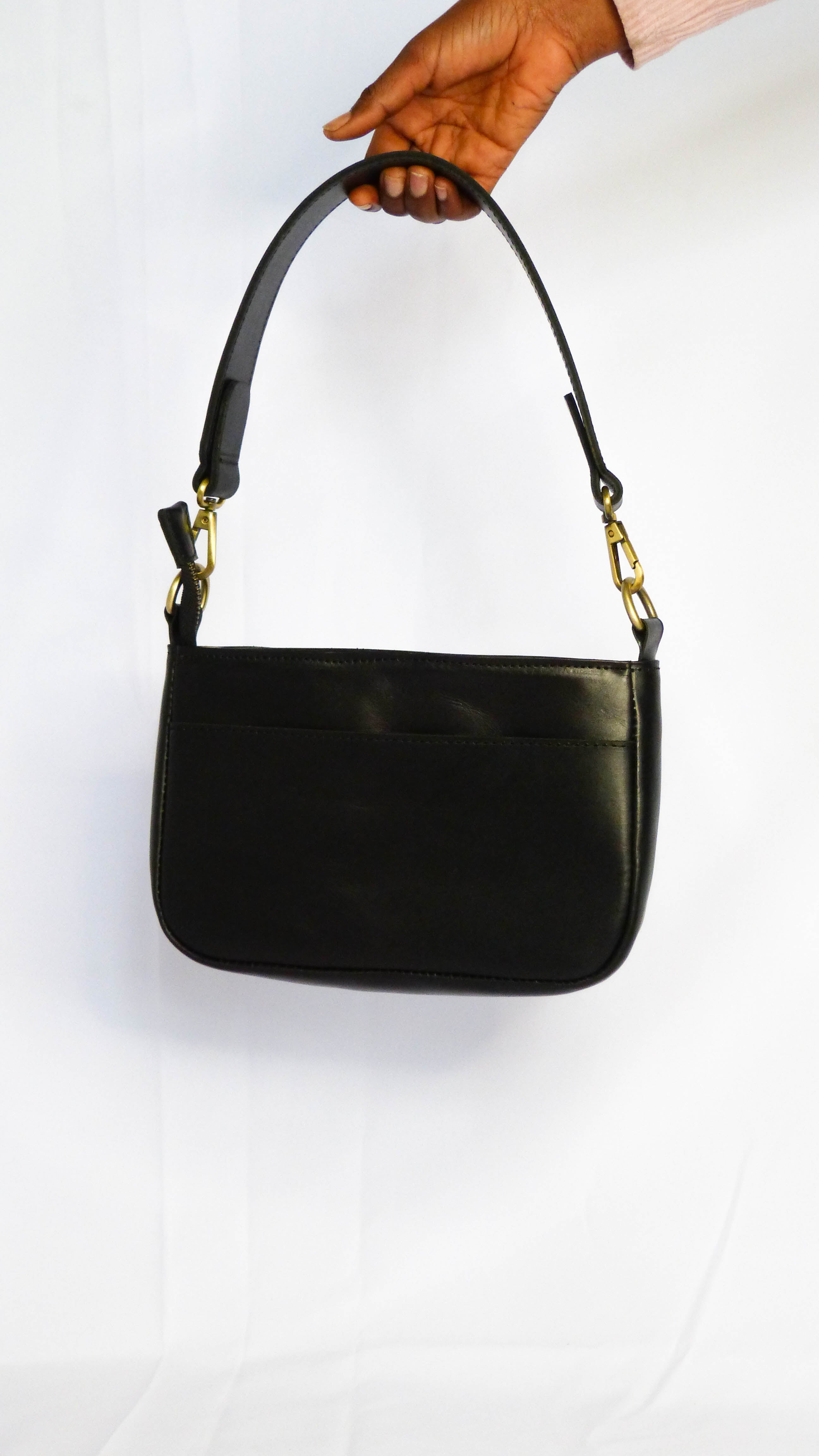 A black leather Jessica purse with gold accents, featuring a removable shoulder strap, zippered top, inside and outside pockets. Handmade by Ethiopian artisans with soft leather. Measures 9 x 5.5 x 2.25.