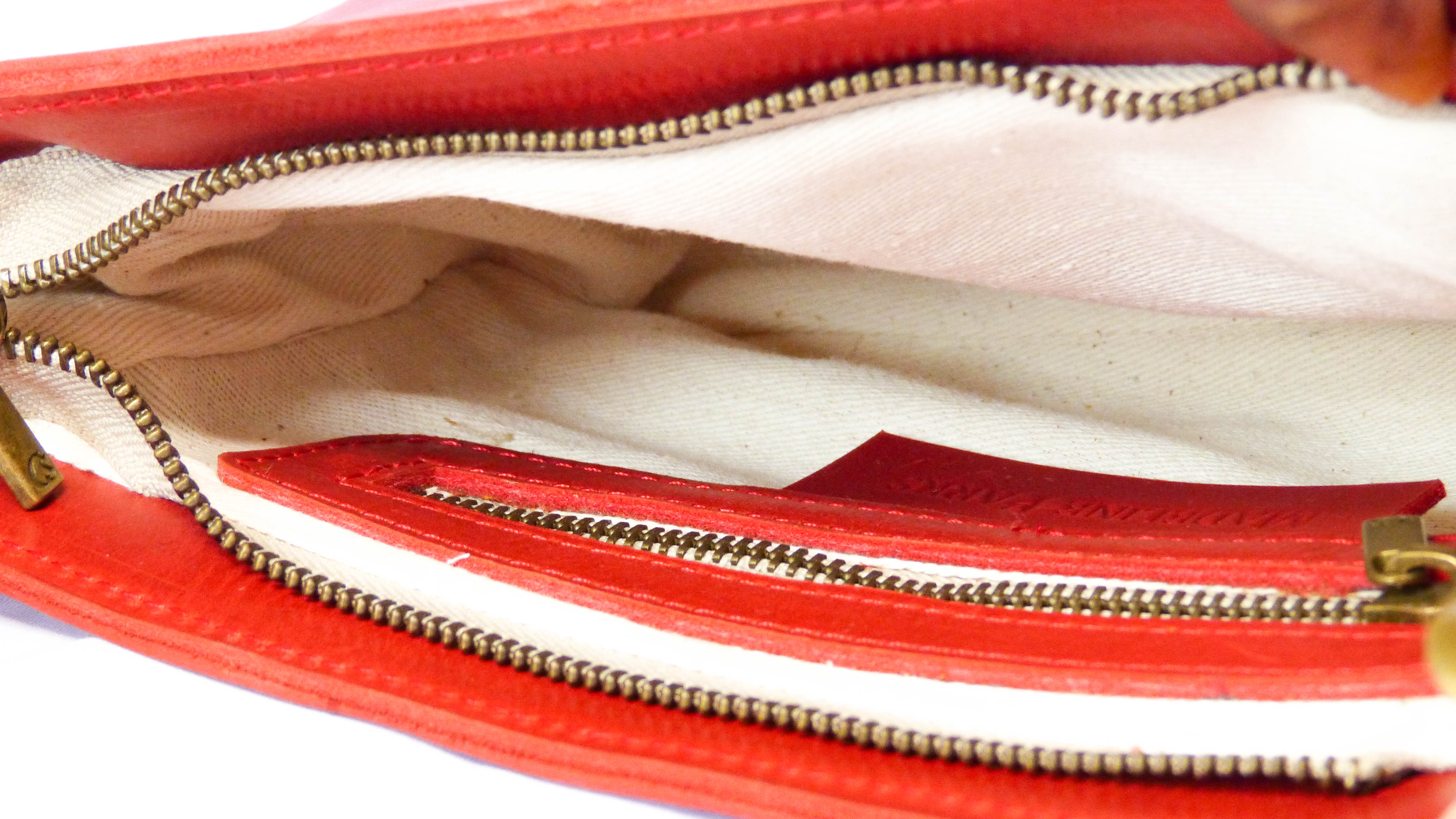 A close-up of the Jessica Leather Purse in Cherry, showcasing intricate zippers and soft leather craftsmanship. Handmade by Ethiopian artisans, featuring a removable shoulder strap and practical pockets for phone storage.