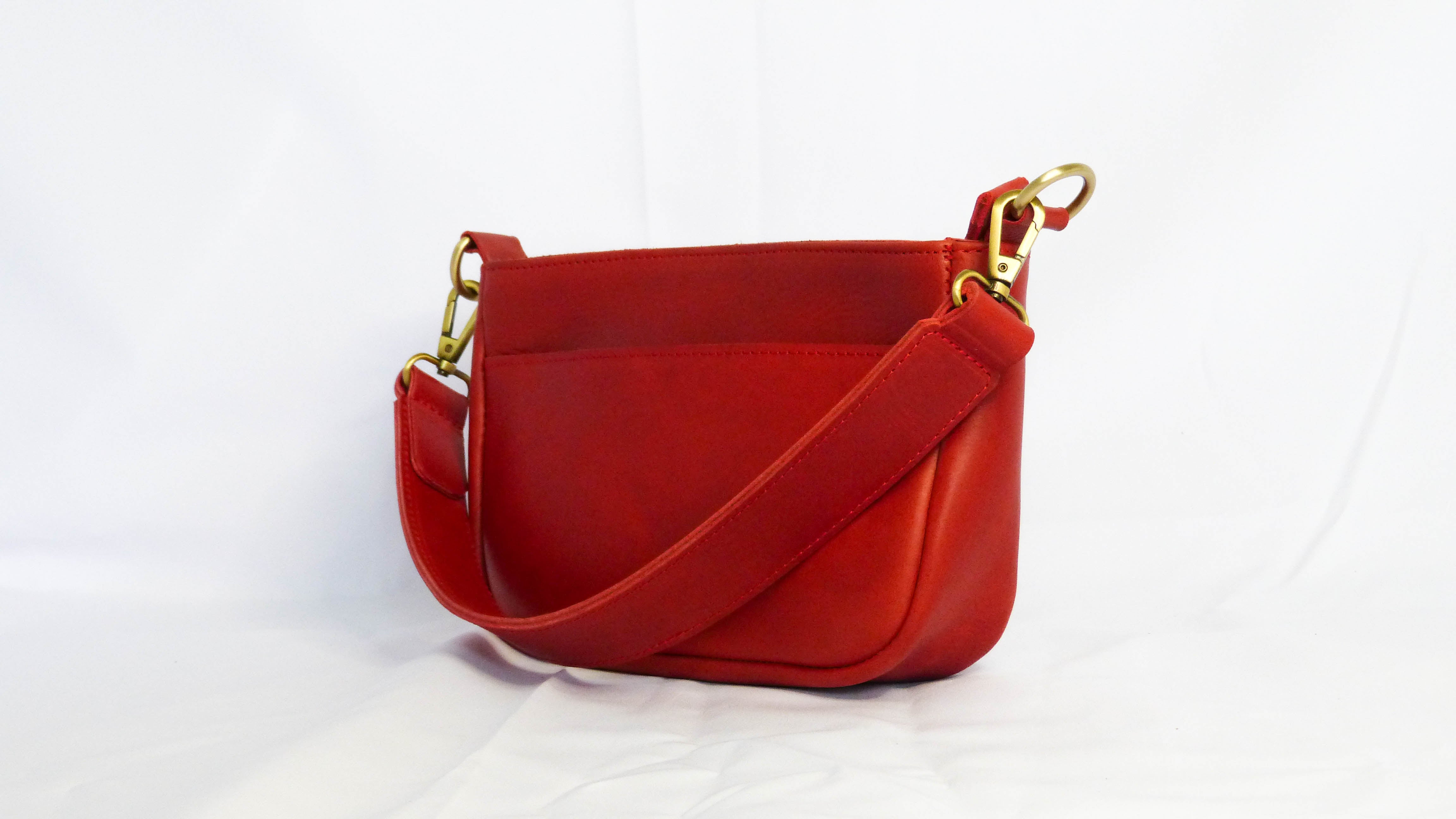 A red leather purse with a removable shoulder strap, zippered top, inside zipper pocket, and outside phone pocket. Handmade by Ethiopian artisans for Madeline Parks Designs.