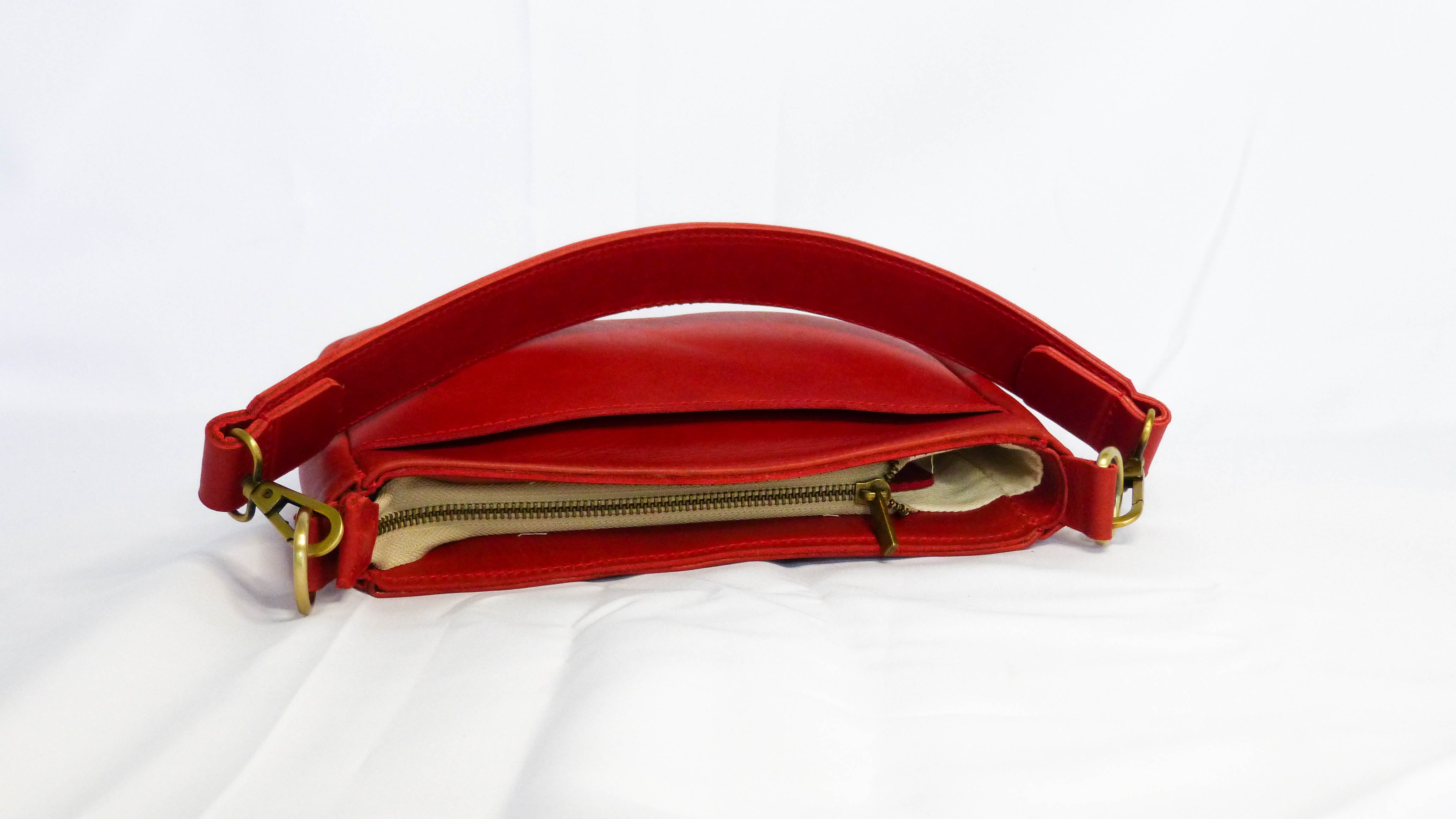 A red leather purse with a handle and zipper, showcasing craftsmanship by Ethiopian artisans. Features a zippered top, inside pocket, and removable shoulder strap. Ideal for everyday use or a night out.