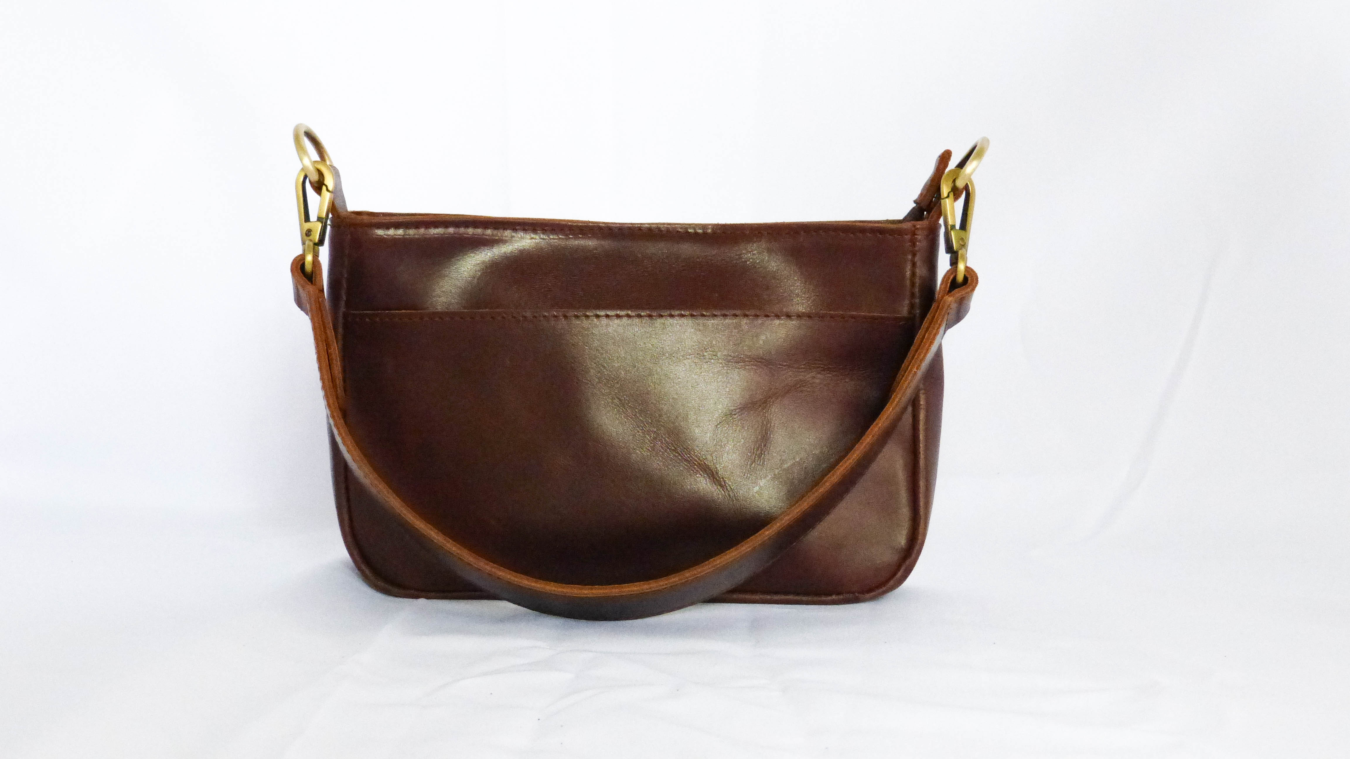 A brown leather purse with gold handles and a removable shoulder strap. Features zippered top, inside zipper pocket, and outside phone pocket. Handmade by Ethiopian artisans. Dimensions: 9 x 5.5 x 2.25.