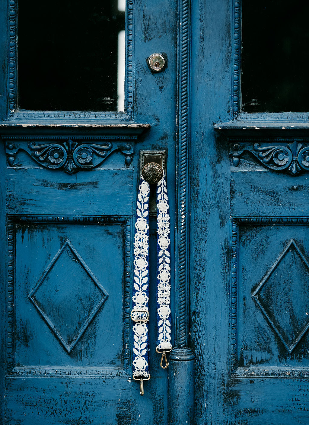 Tess Adjustable Strap displayed hanging on the doorknob of a blue door.